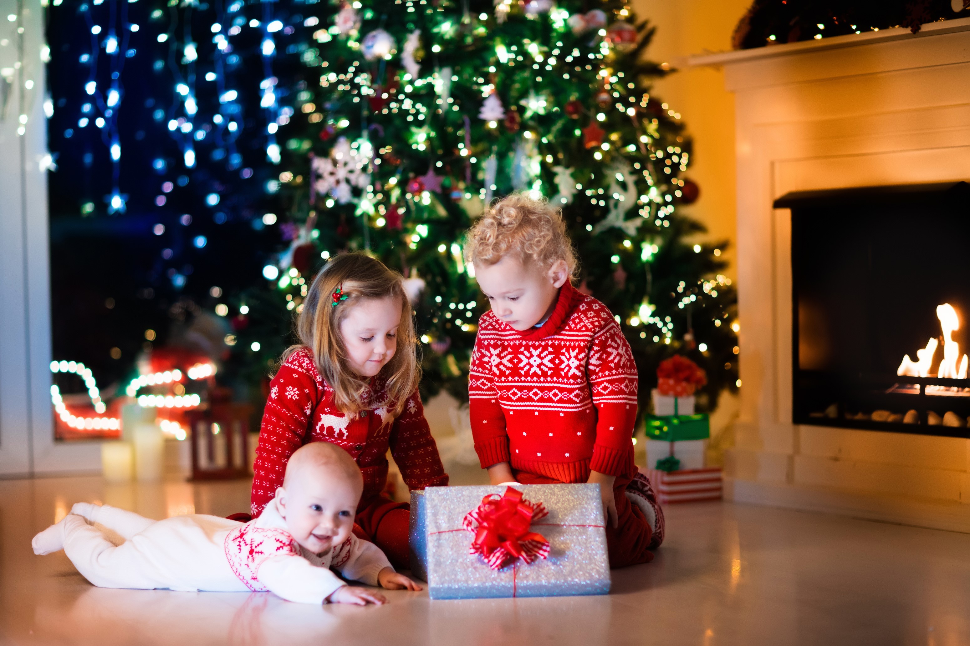 Three Children Opening Christmas Gifts by the Tree HD Wallpaper