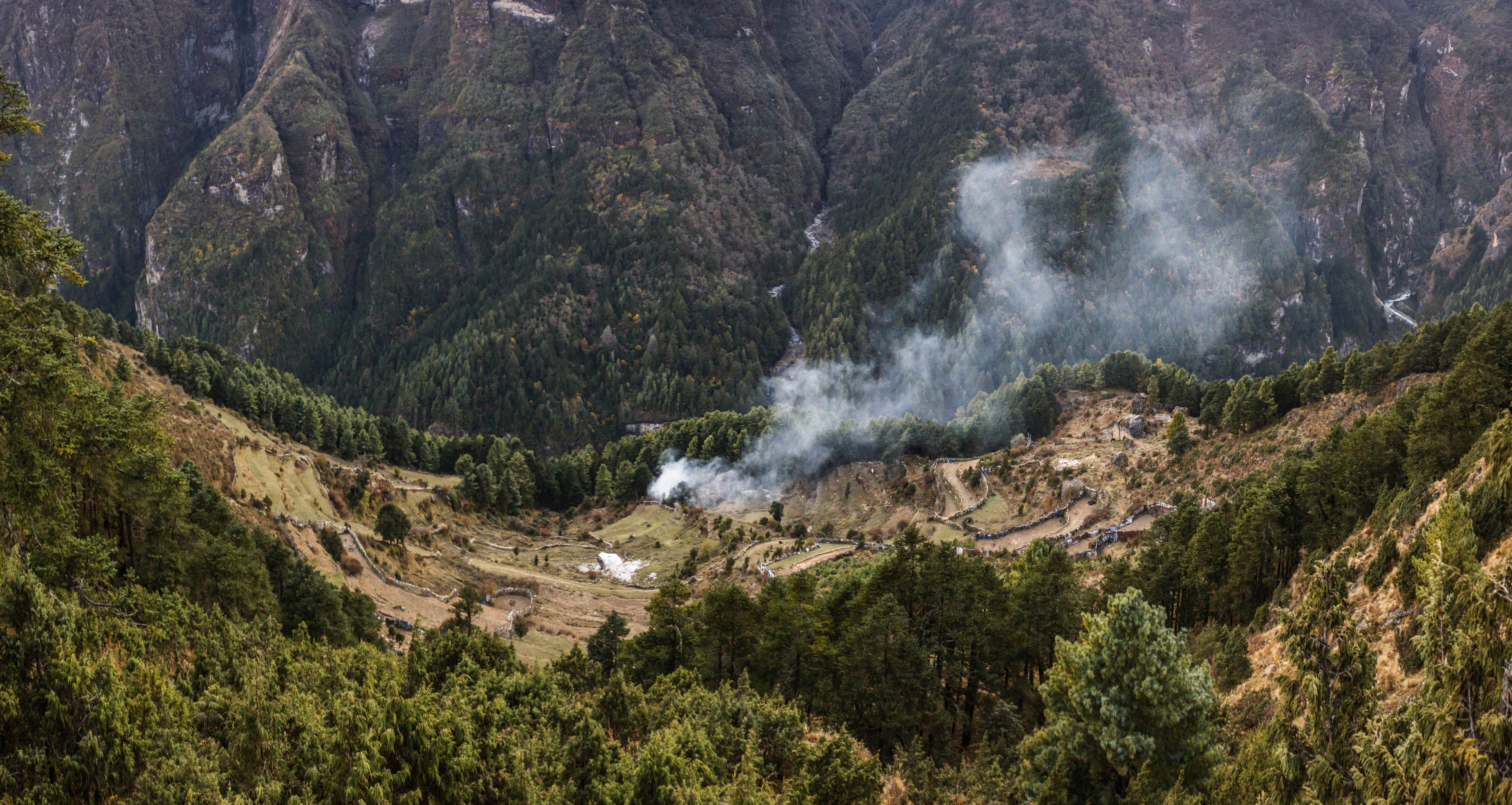 Smoke rising from a village in a forested mountain valley in Nepal HD Wallpaper