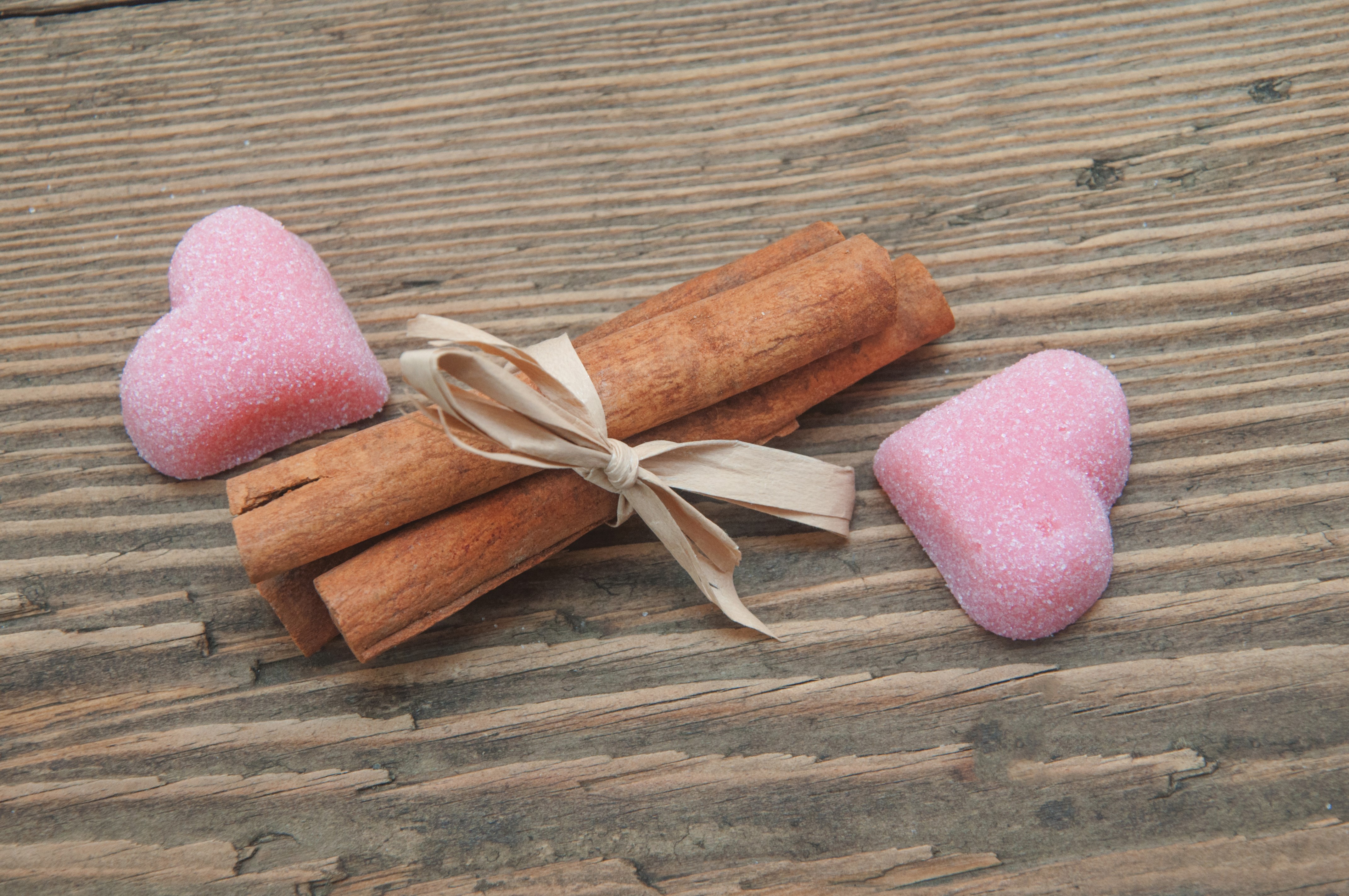 Cinnamon sticks with pink heart candies on wood HD Wallpaper