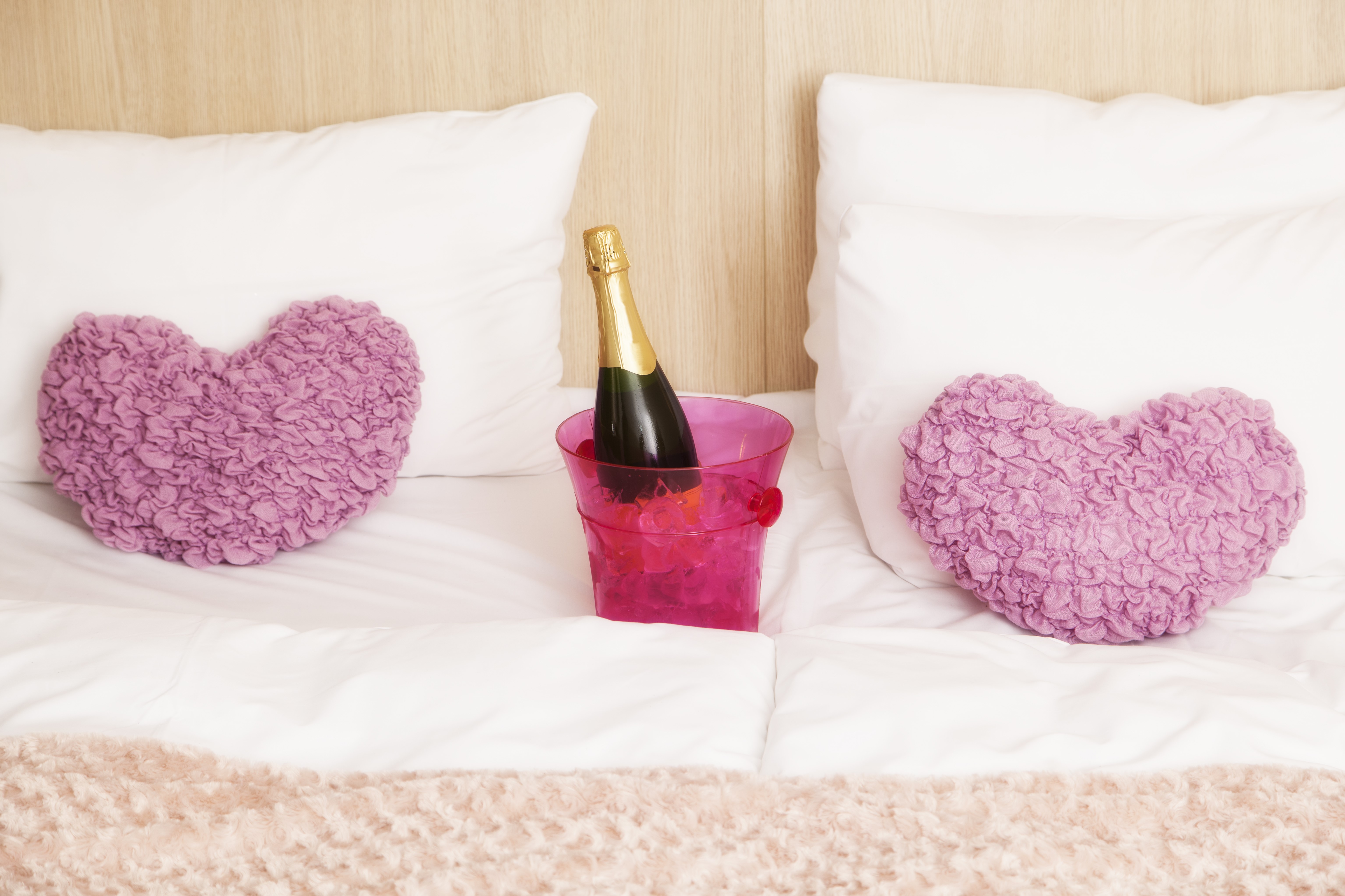 Champagne bottle between heart pillows on a bed HD Wallpaper