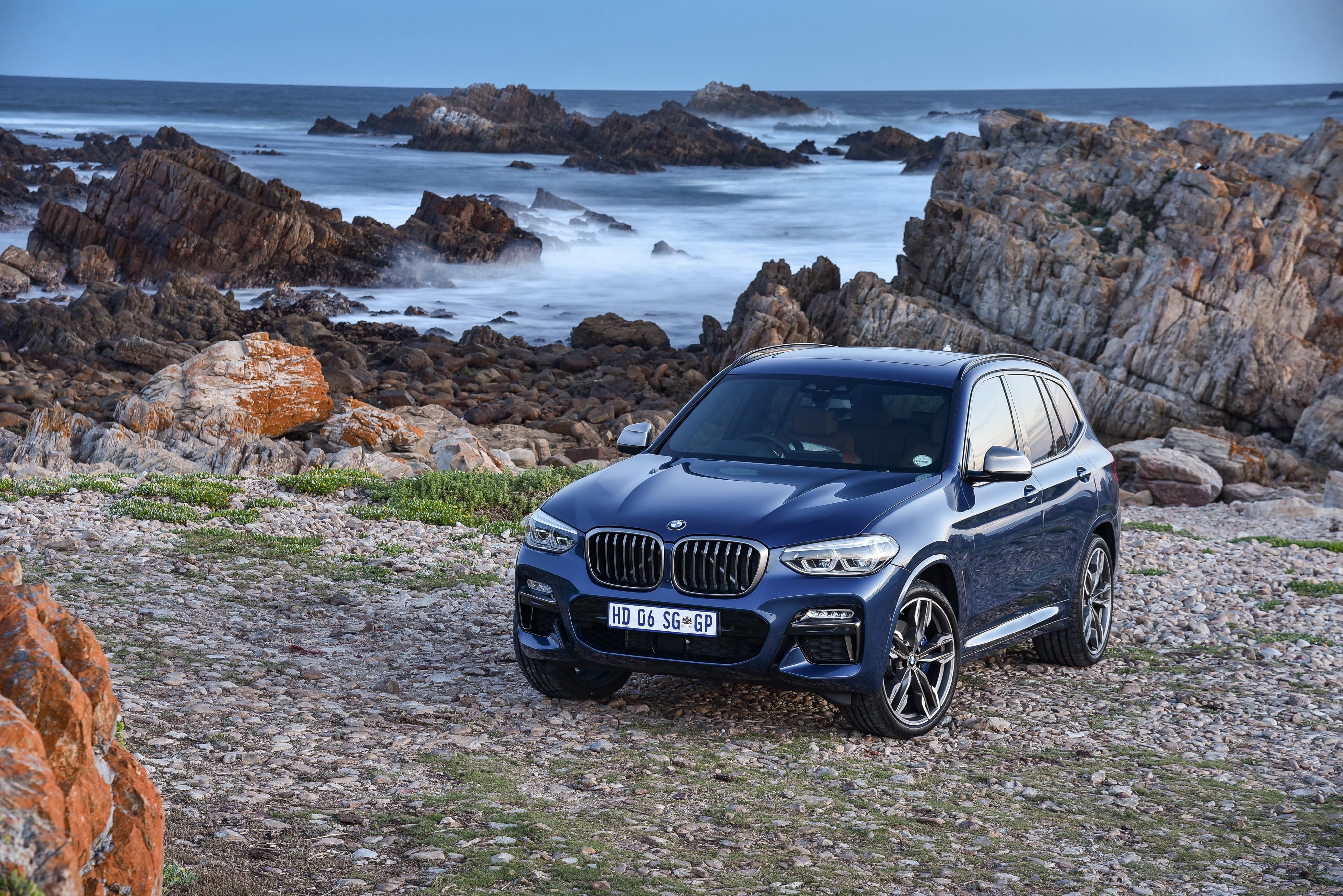 Blue BMW X3 M40i parked on rocky shore HD Wallpaper