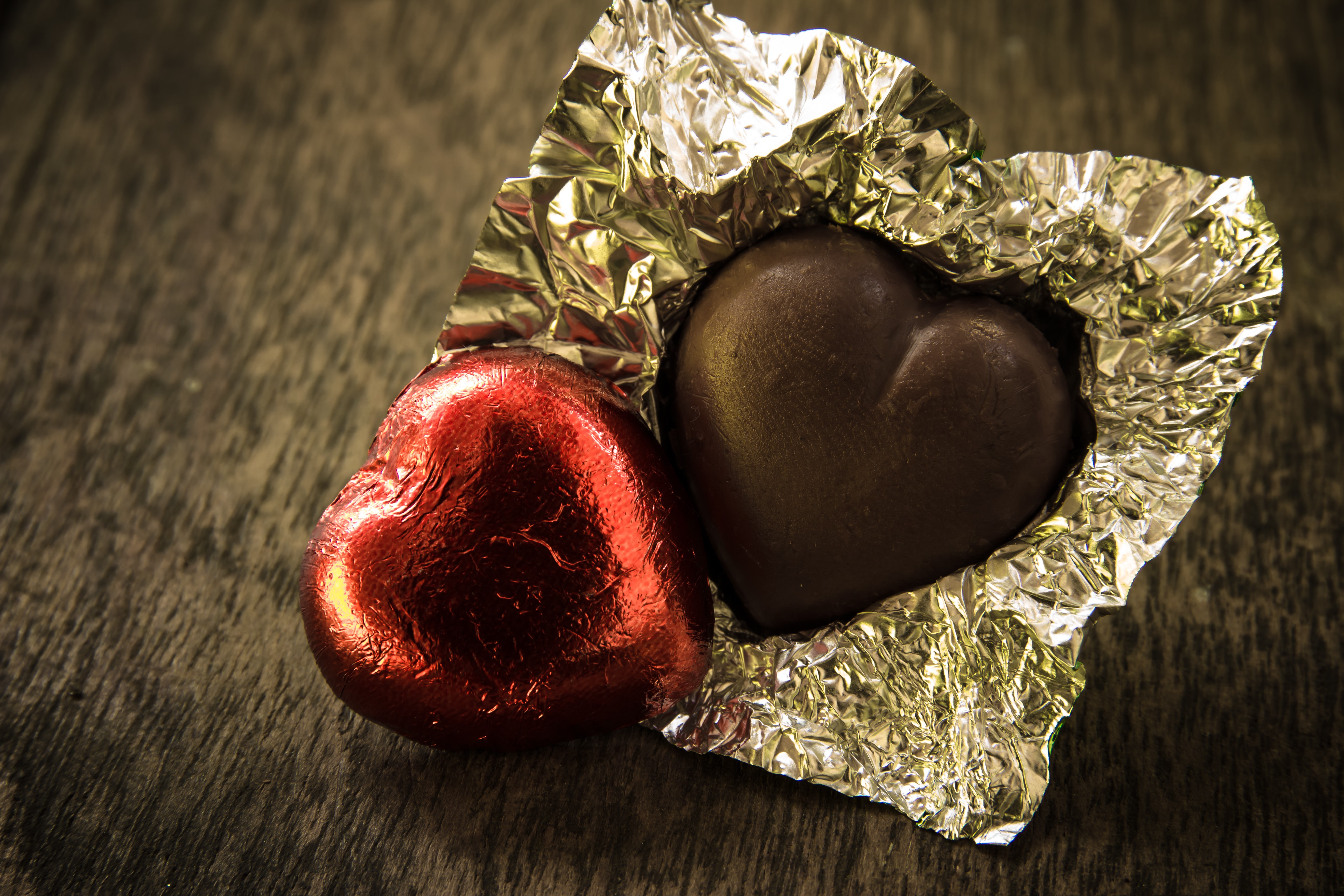 Two heart-shaped chocolates, one red, one dark, on a wooden surface HD Wallpaper