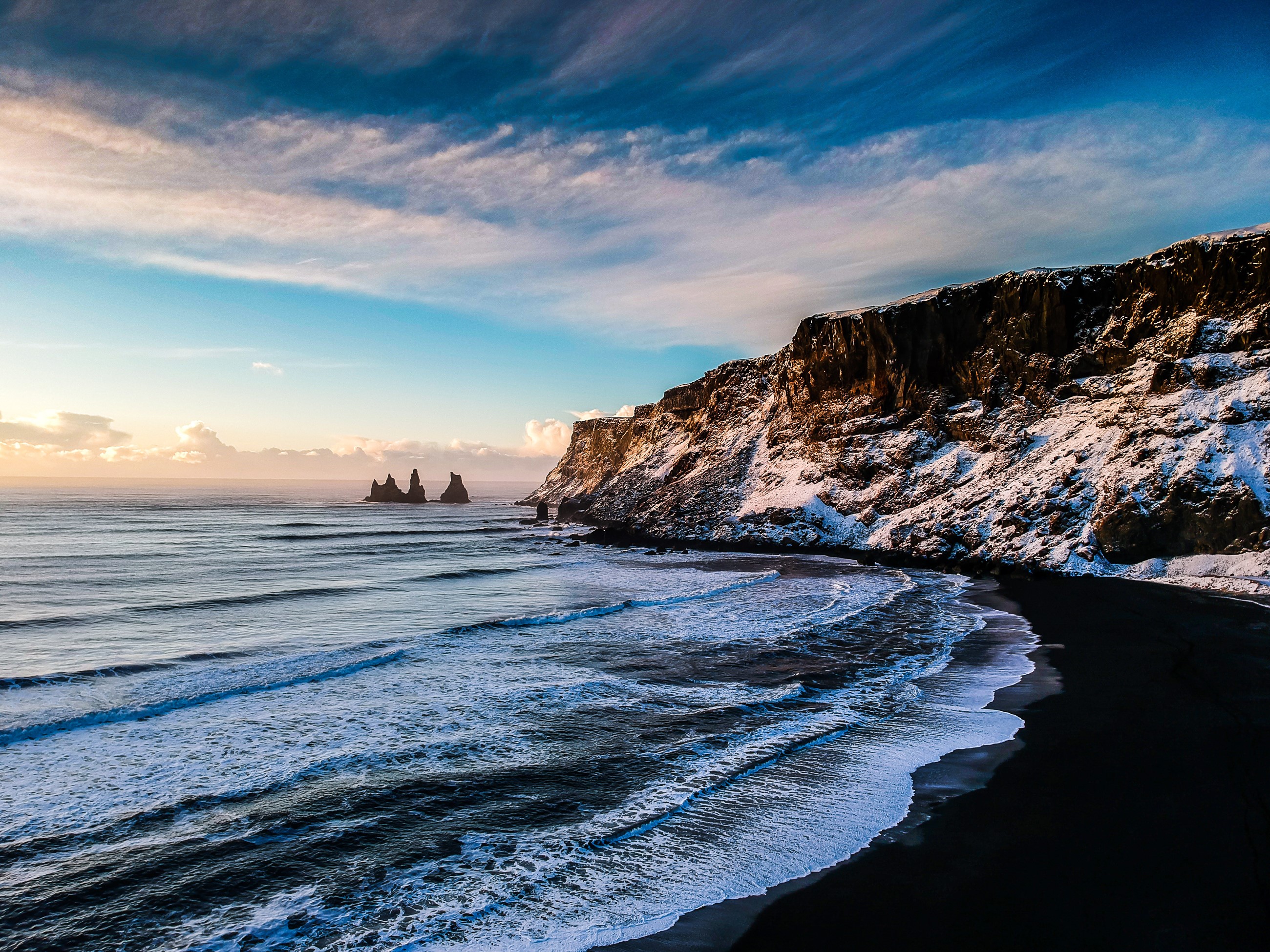 Black sand beach with snow-covered cliffs and sea stacks in Iceland HD Wallpaper
