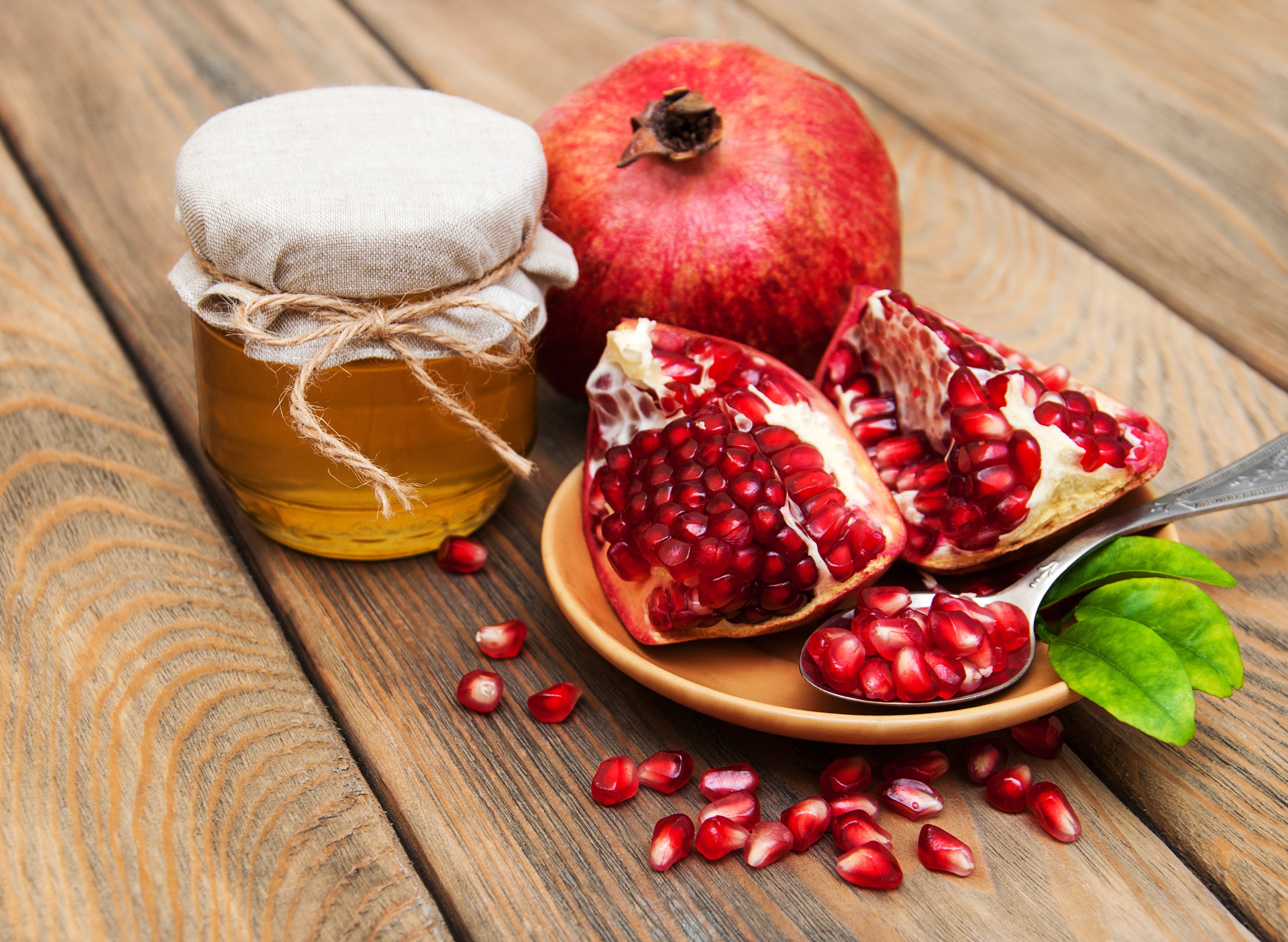 Honey jar and pomegranates on wooden planks HD Wallpaper
