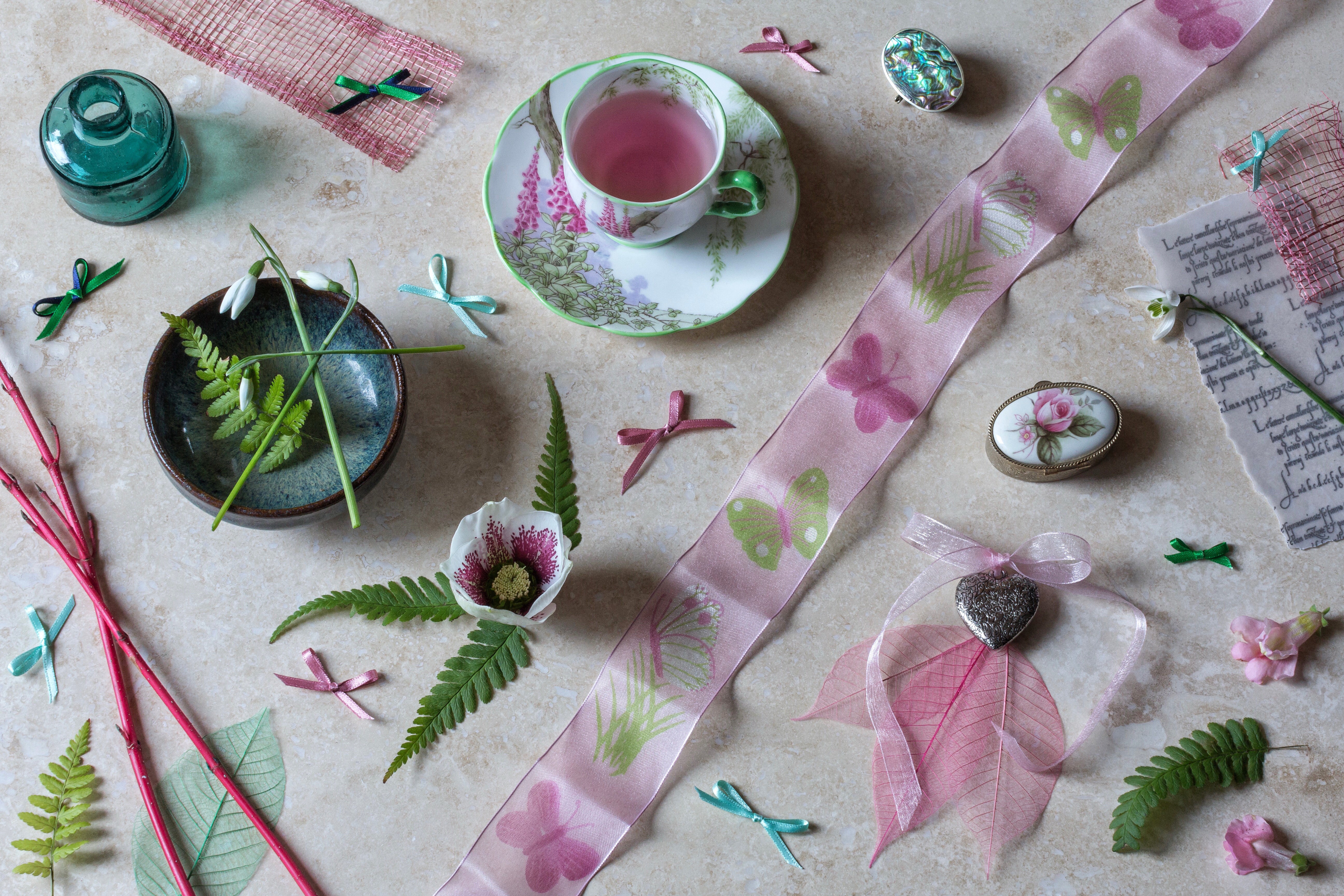 Tea cup with pink liquid and floral saucer, ribbon with butterflies, anemone flower, snowdrops, fern, and decorative items HD Wallpaper