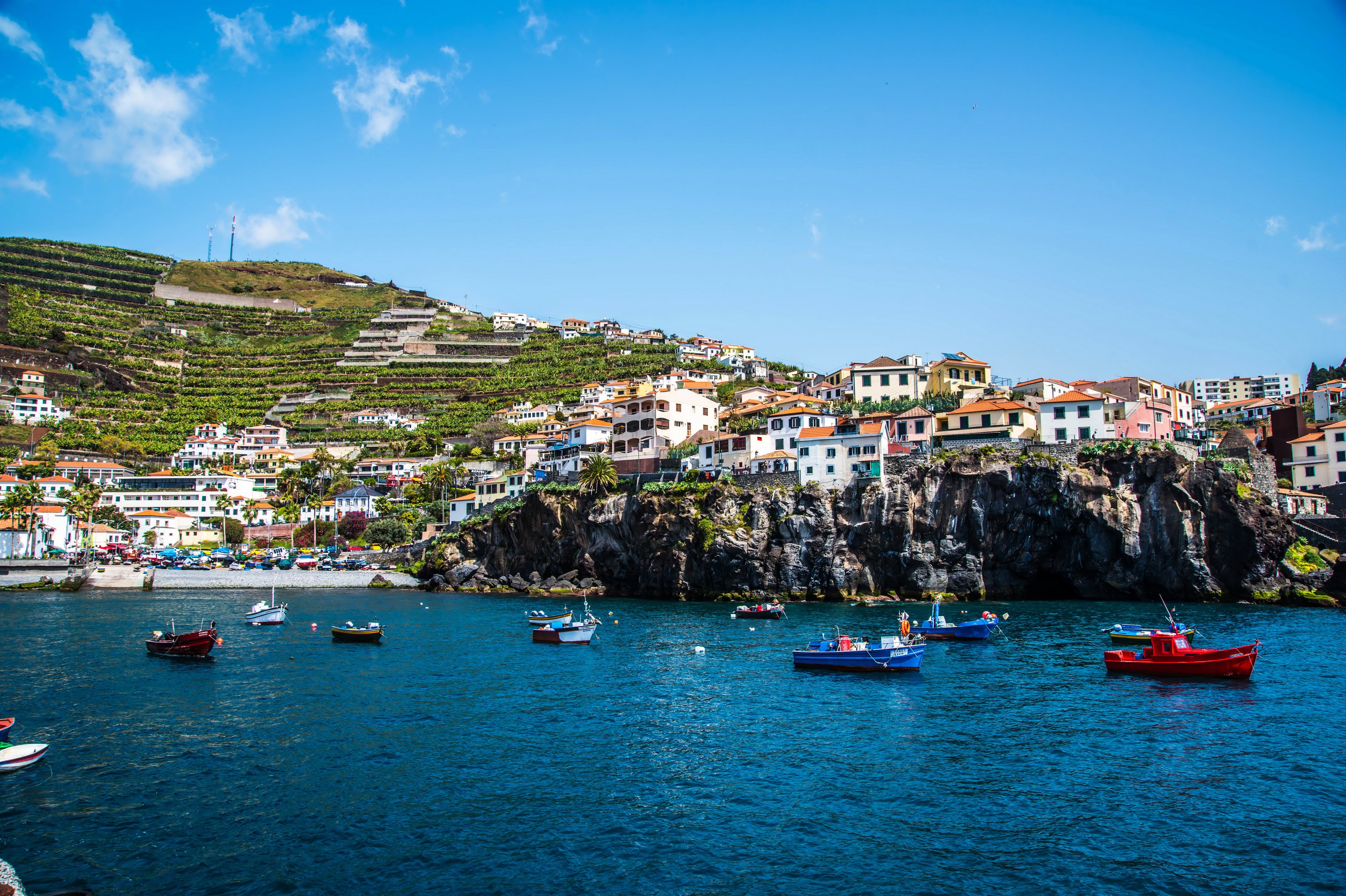 Boats in a harbor with a coastal town on a hillside HD Wallpaper
