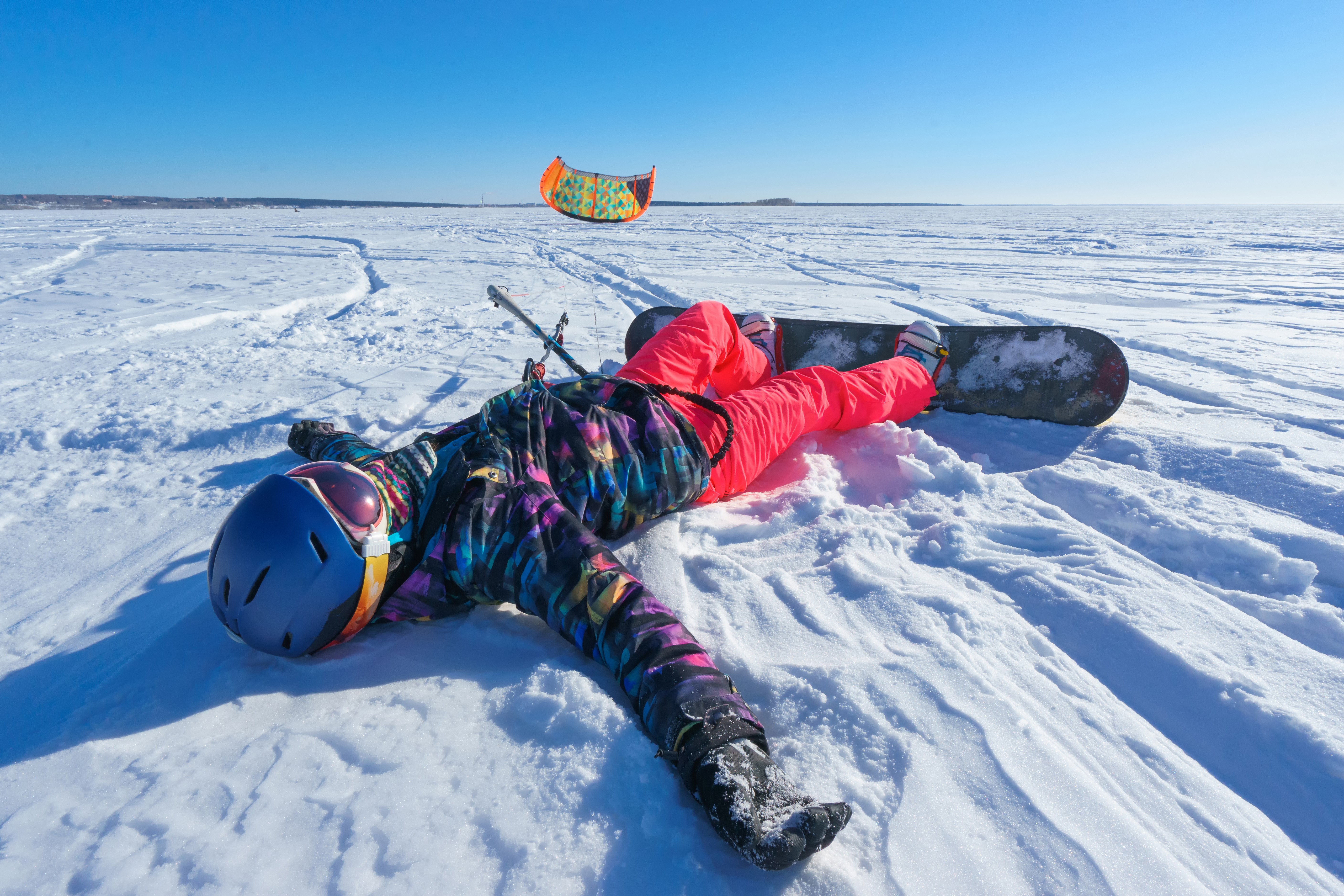 Snowboarder lying on snow with kite in the air HD Wallpaper
