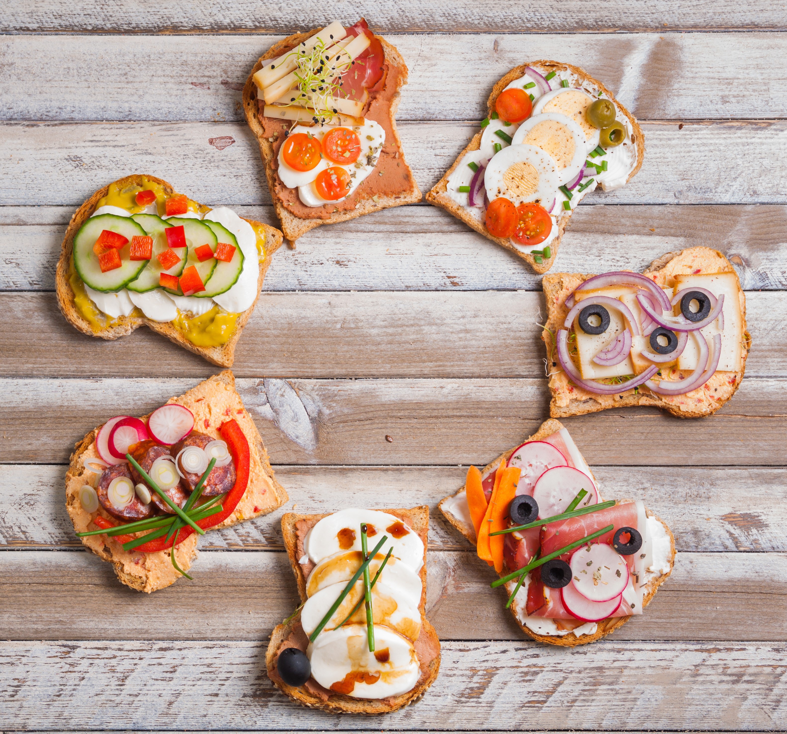 Assortment of open-faced sandwiches with various toppings on wooden table HD Wallpaper