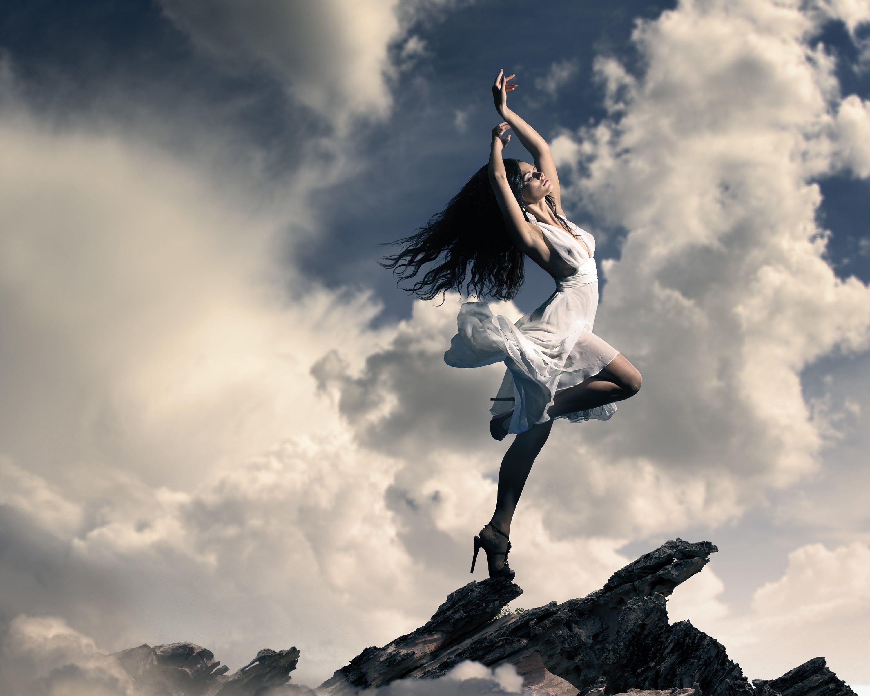 Woman in white dress dancing on rocks with clouds HD Wallpaper