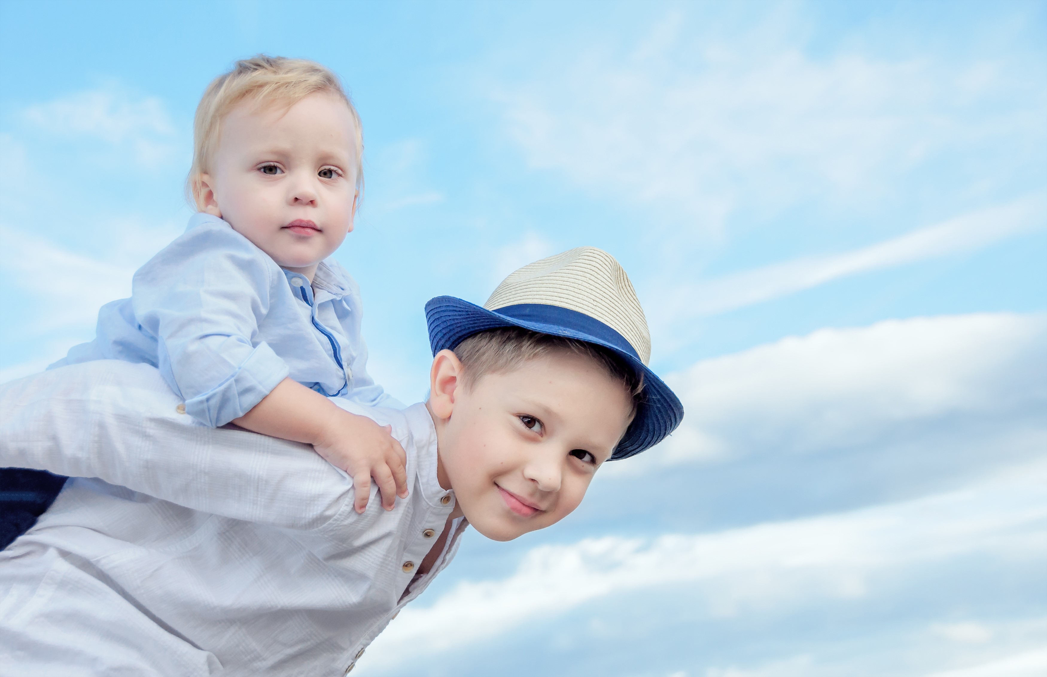 Two boys, one on the other's shoulders, against a blue sky HD Wallpaper