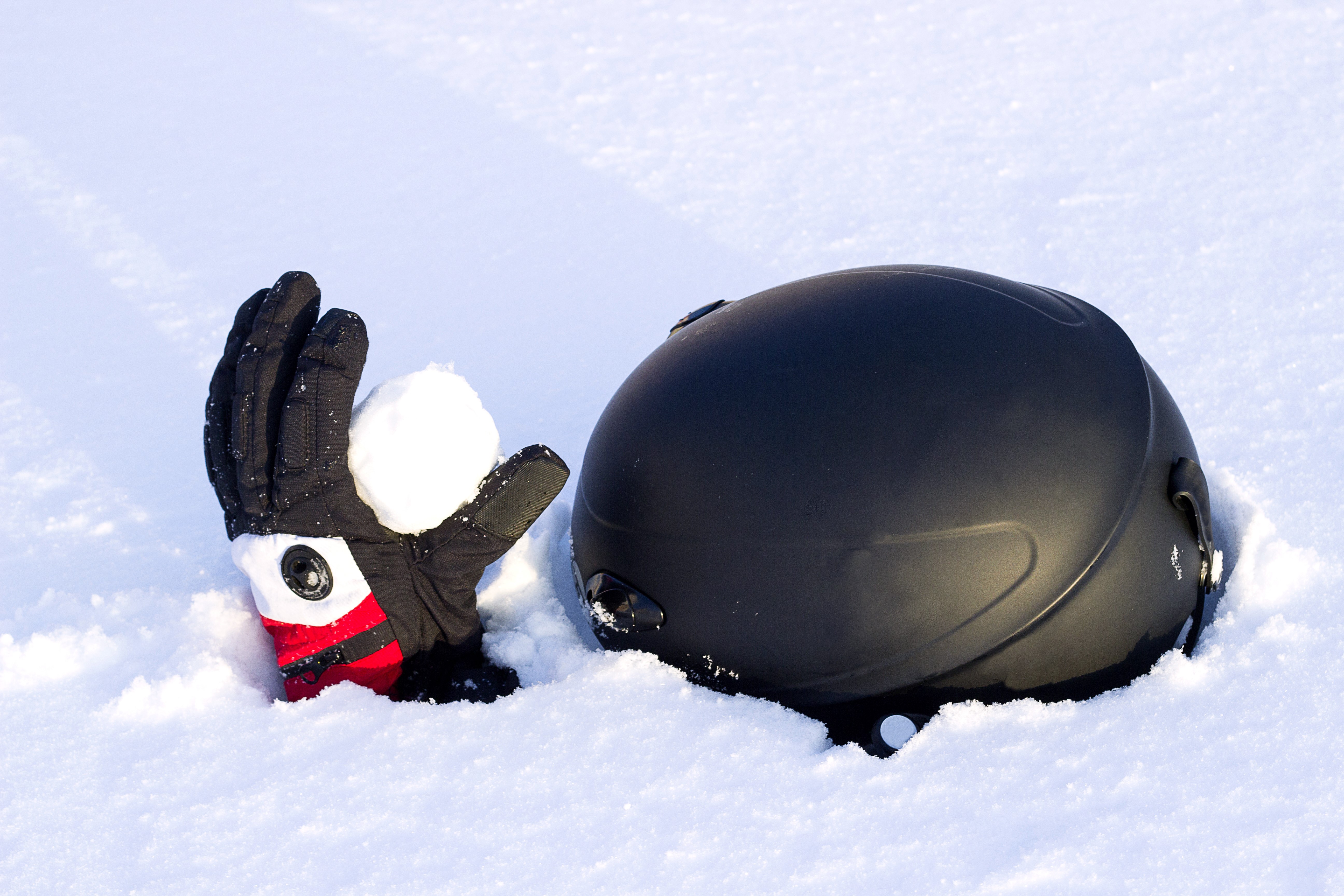 Glove holding snowball next to ski helmet in snow HD Wallpaper
