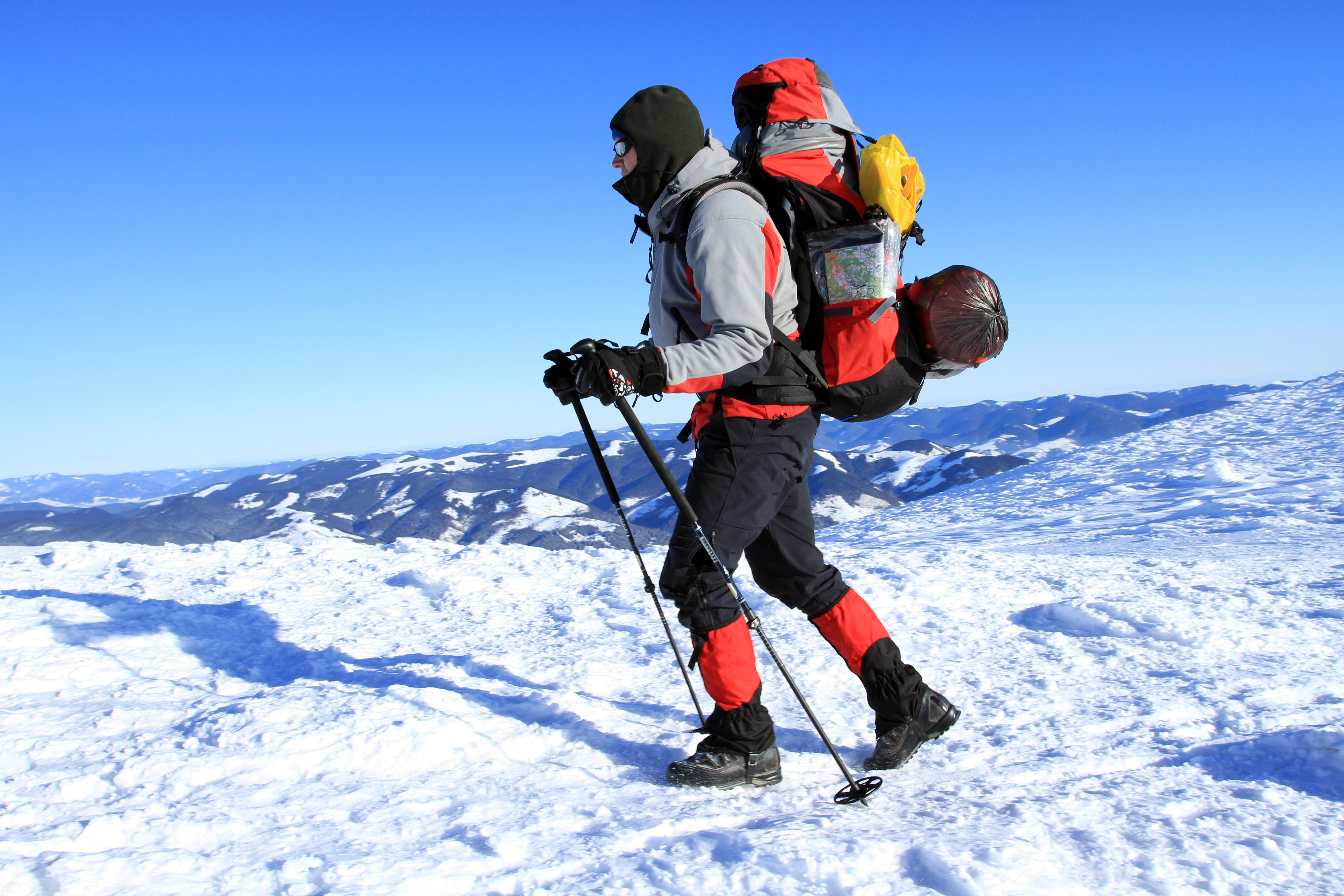 Man hiking in snowy mountains with trekking poles HD Wallpaper
