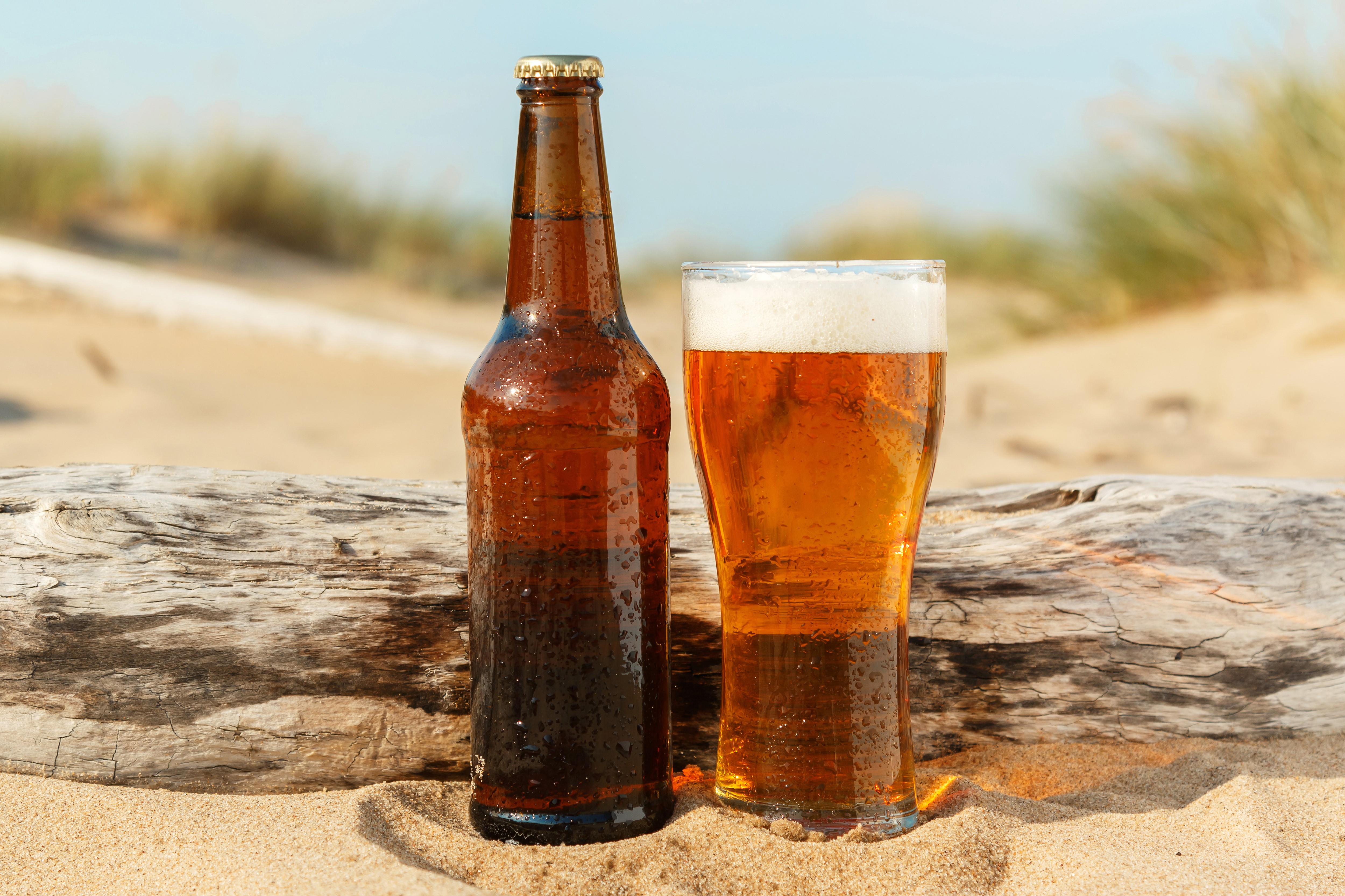 Beer bottle and glass on a beach HD Wallpaper
