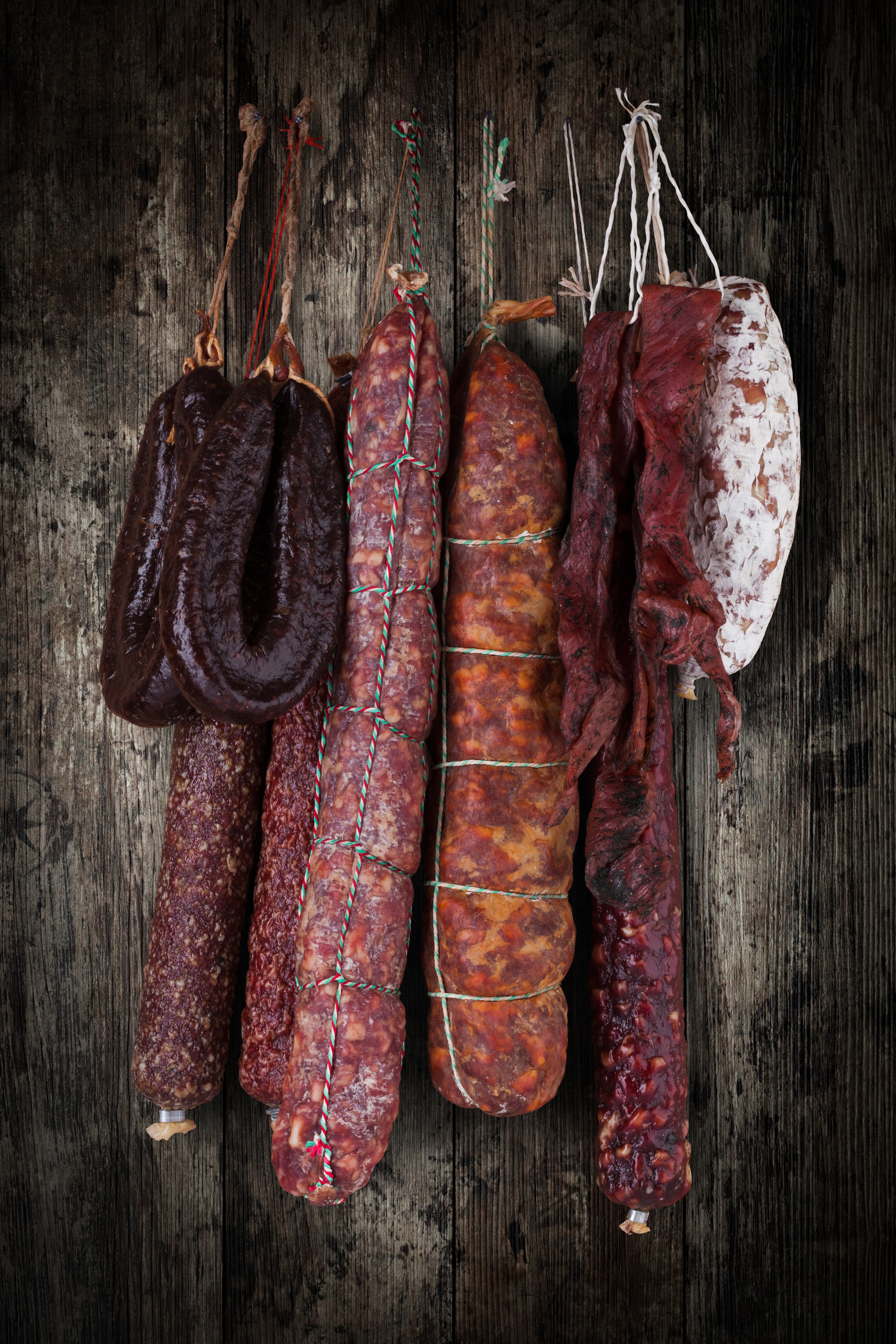 Various cured sausages hanging on a wooden background HD Phone Wallpaper