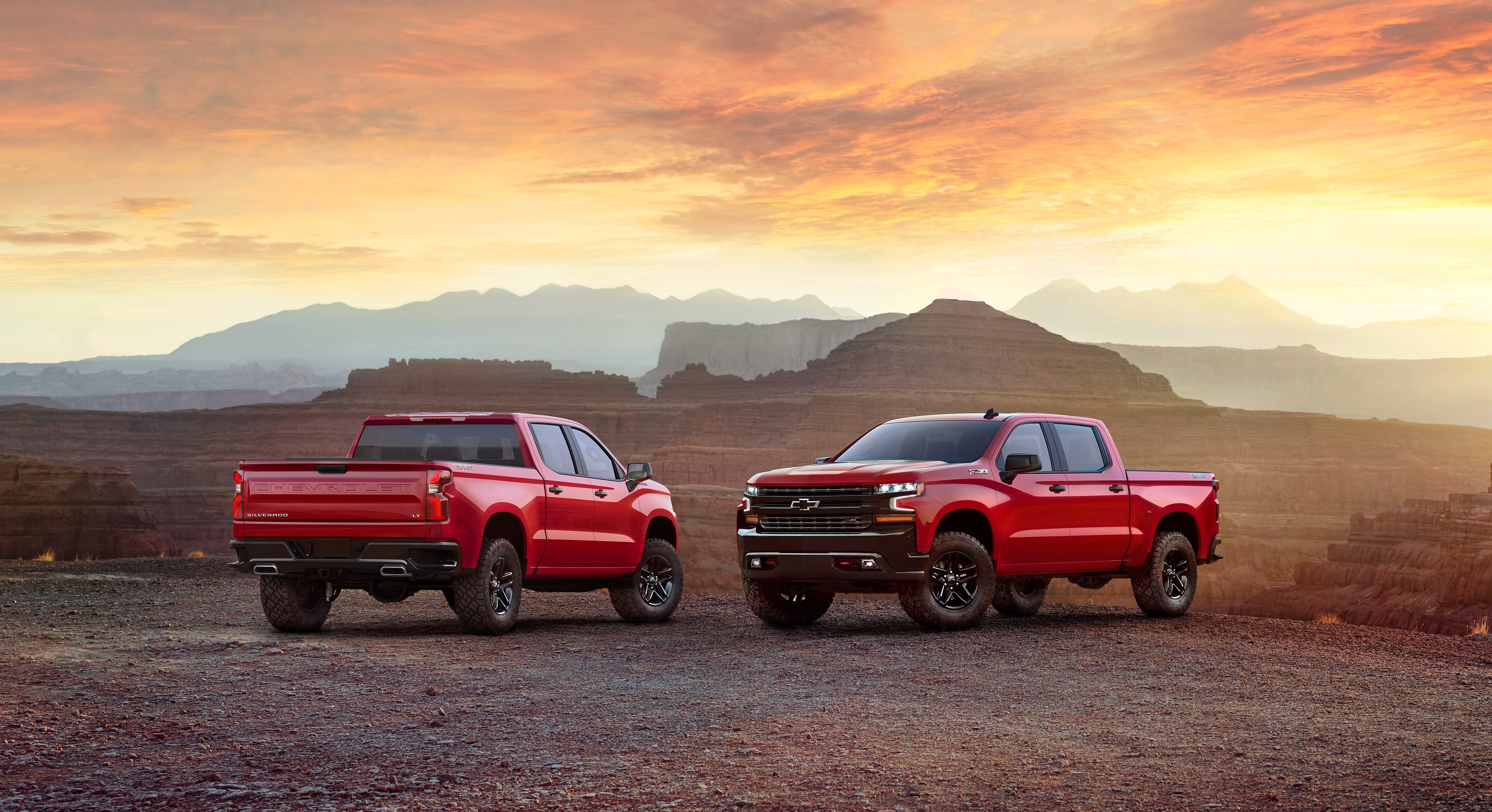 Two red Chevrolet Silverado pickup trucks in a desert landscape HD Wallpaper