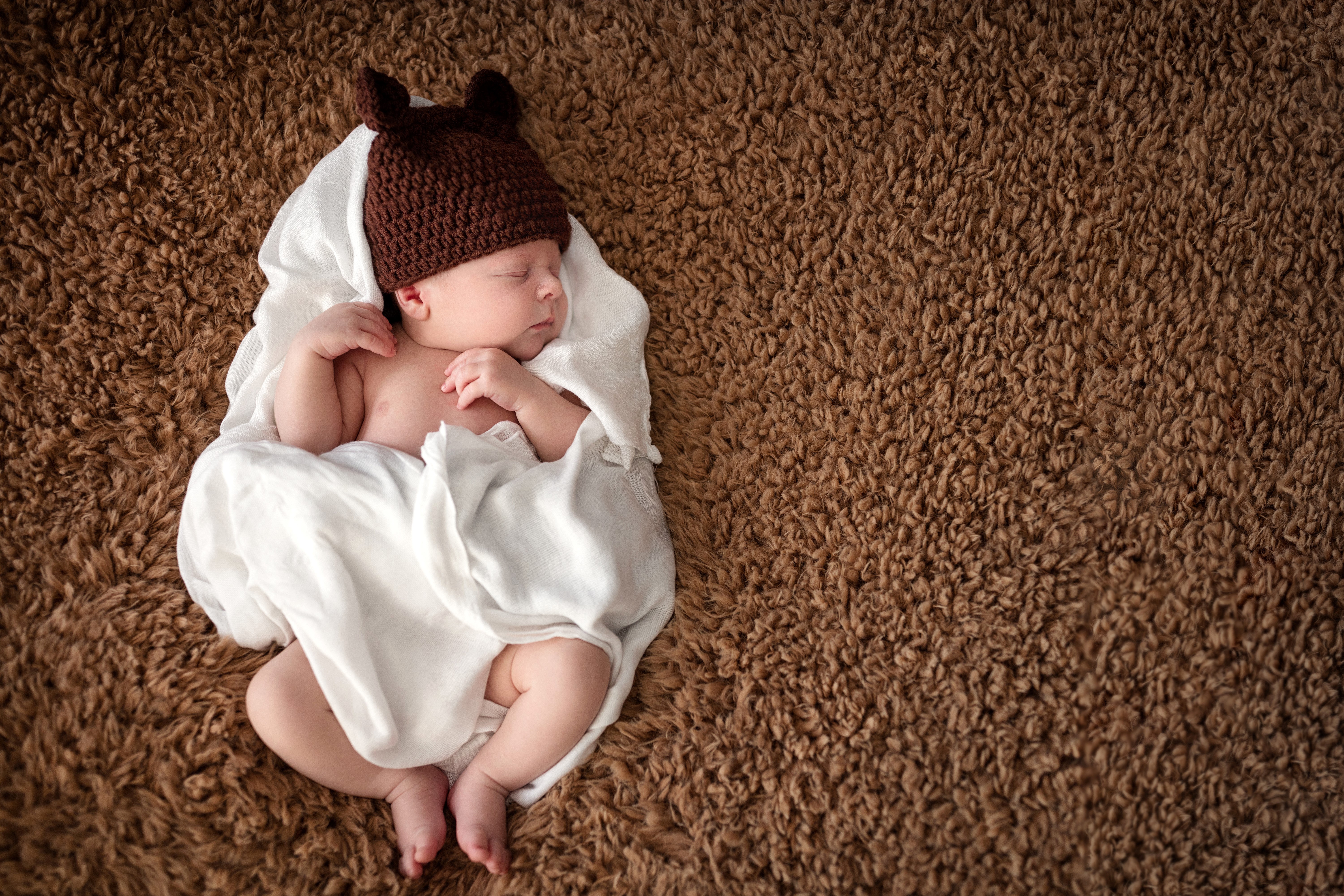 Newborn baby sleeping on a brown carpet wearing a hat HD Wallpaper