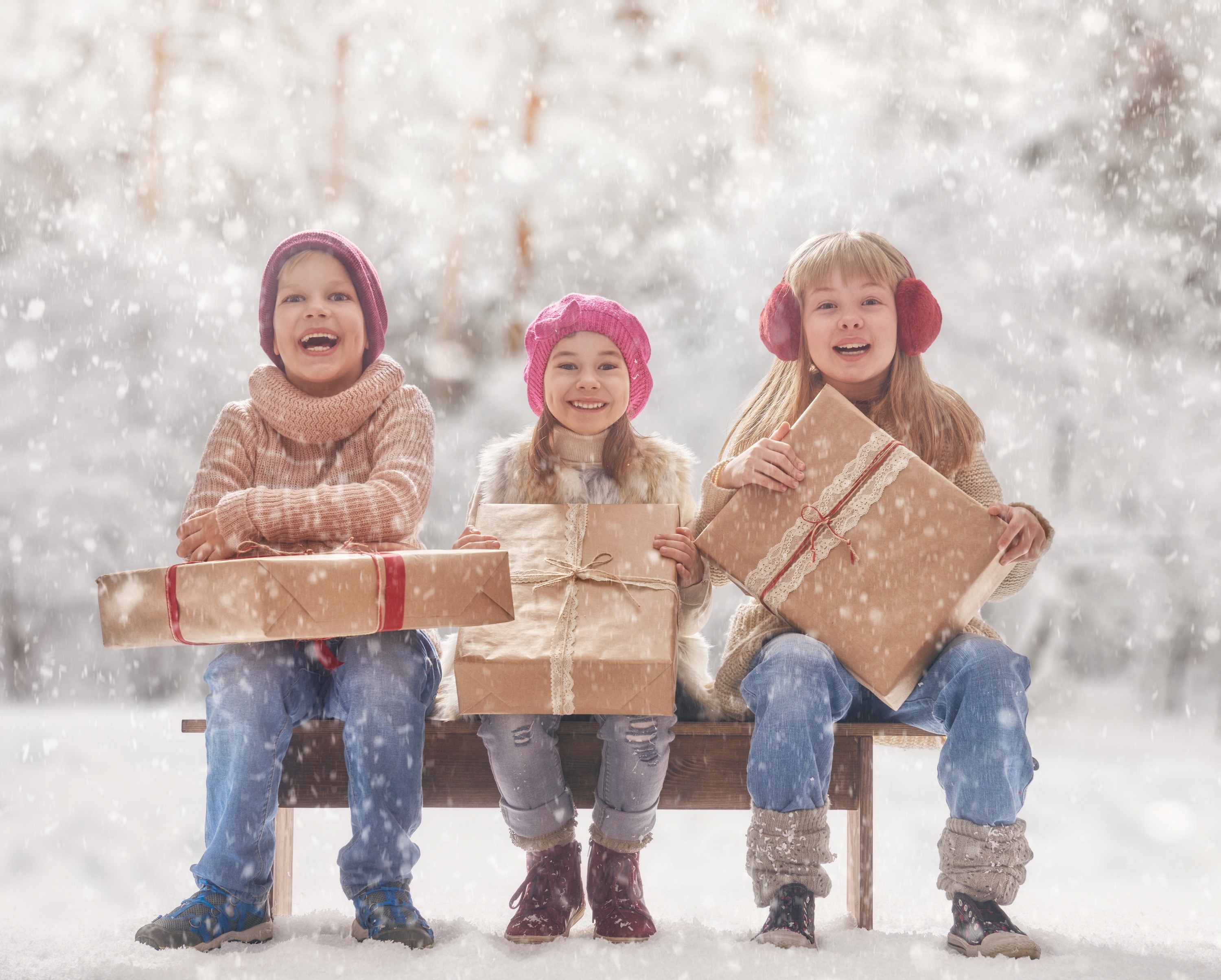 Three children with Christmas gifts in the snow HD Wallpaper