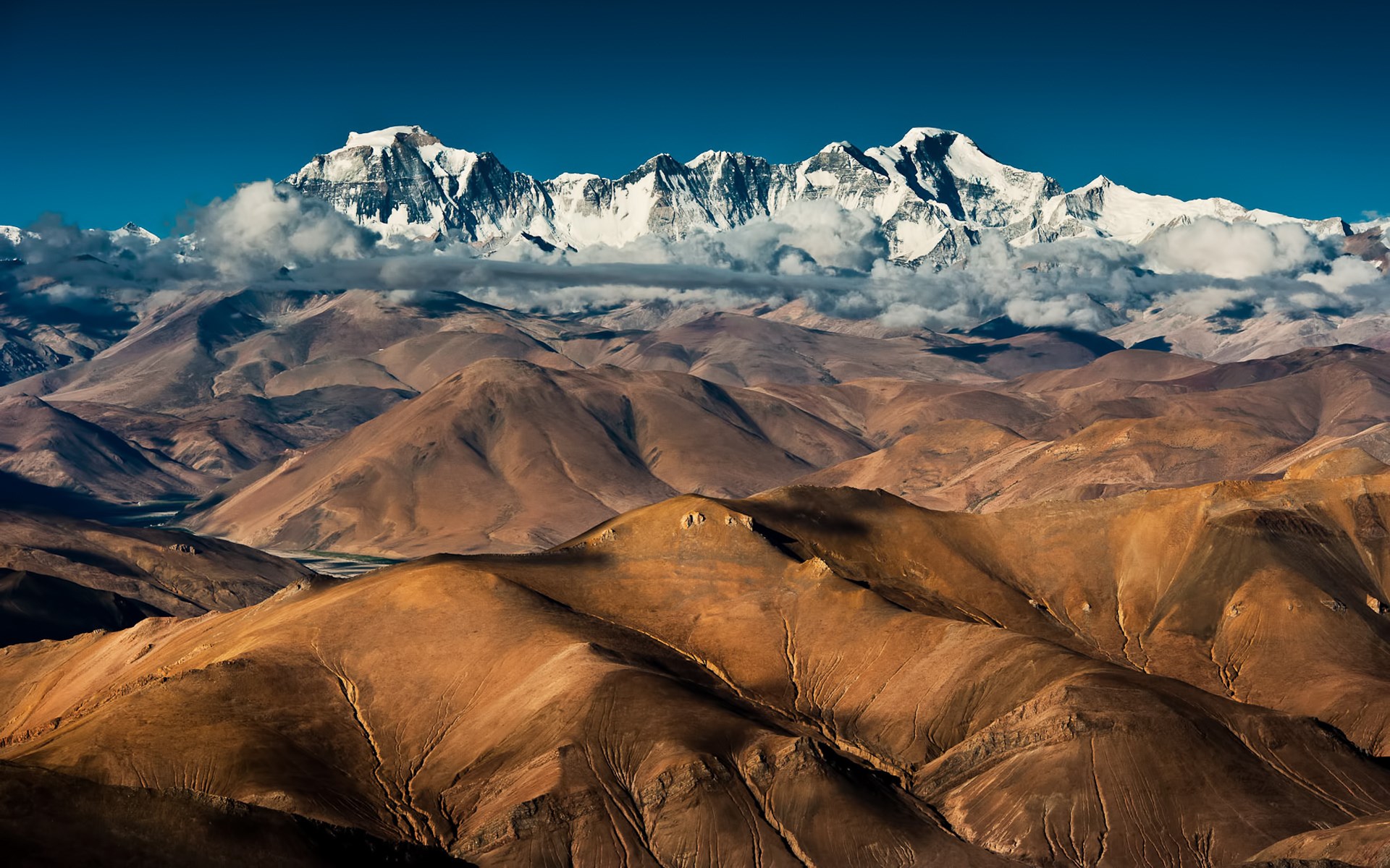 Snow-capped mountains above barren hills under a blue sky HD Wallpaper