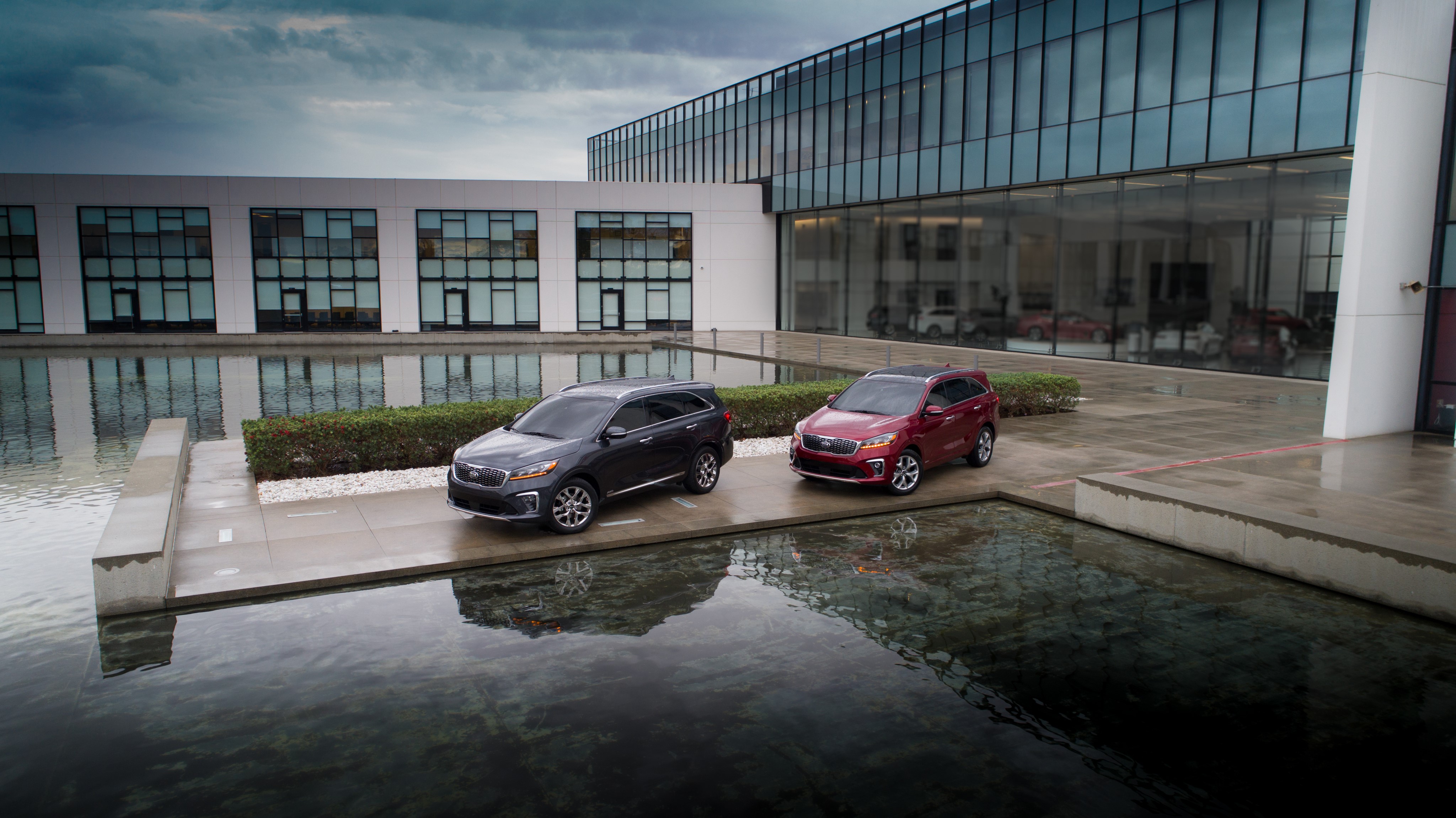 Two Kia Sorento SUVs parked near a modern building HD Wallpaper