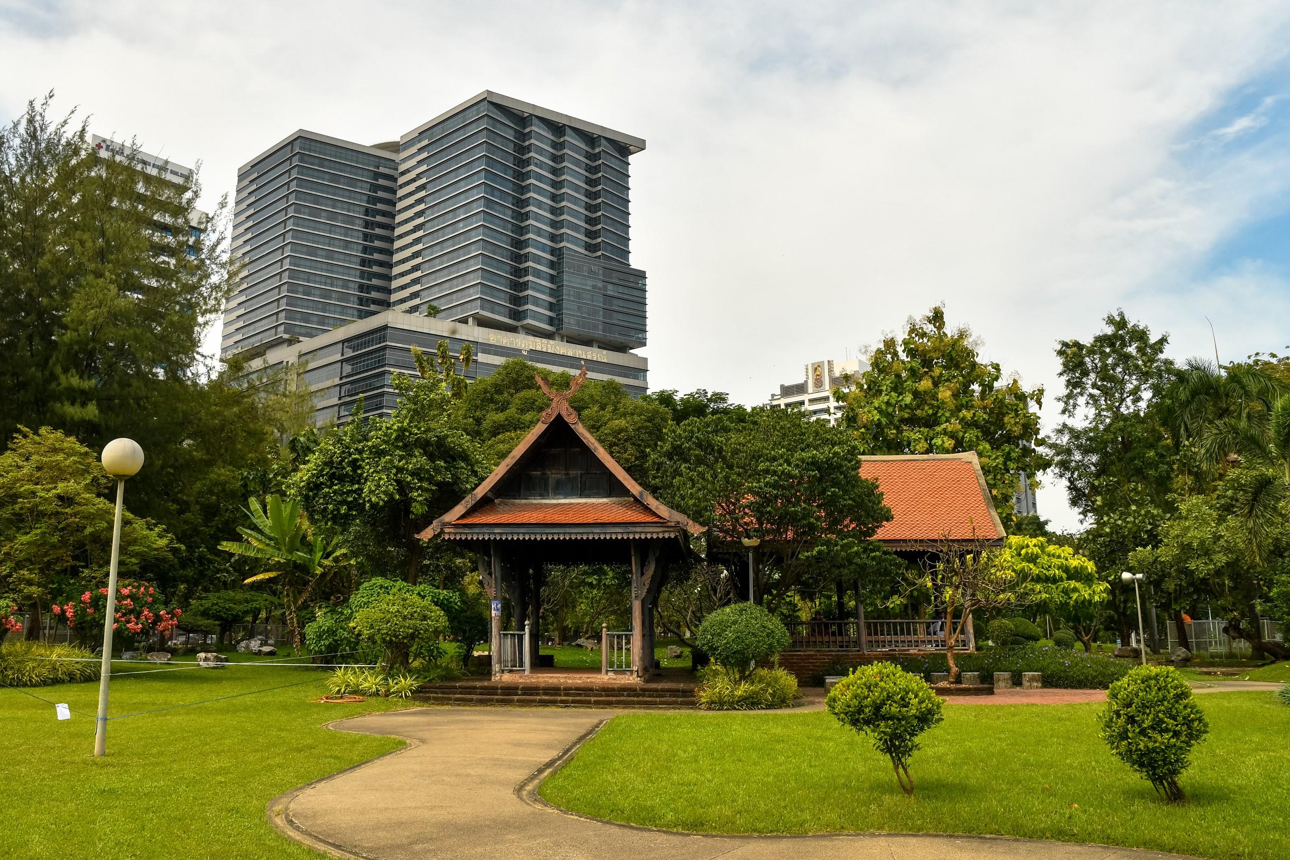 Park with traditional Thai pavilion and modern buildings HD Wallpaper