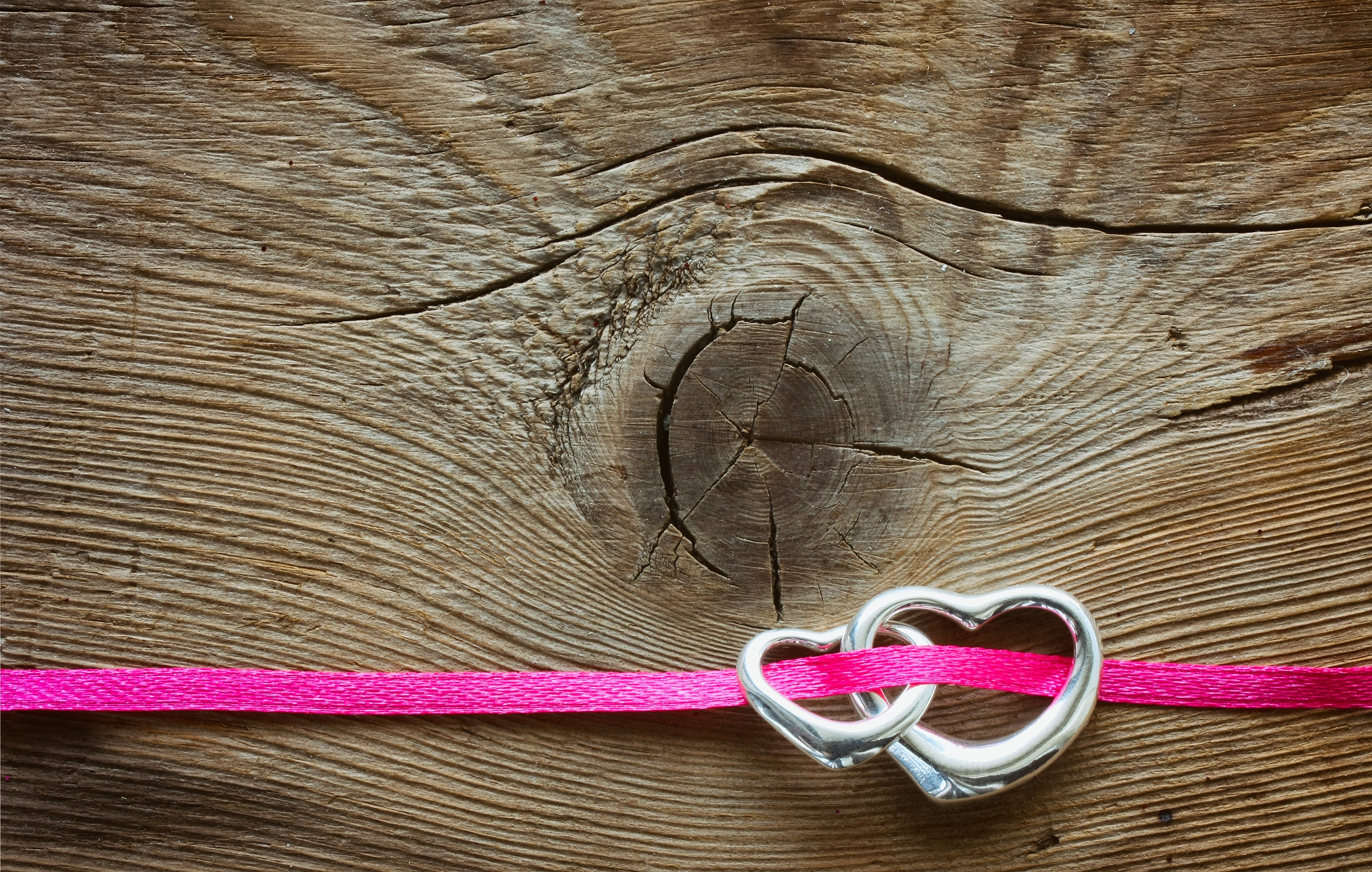 Two hearts intertwined with pink ribbon on wood HD Wallpaper