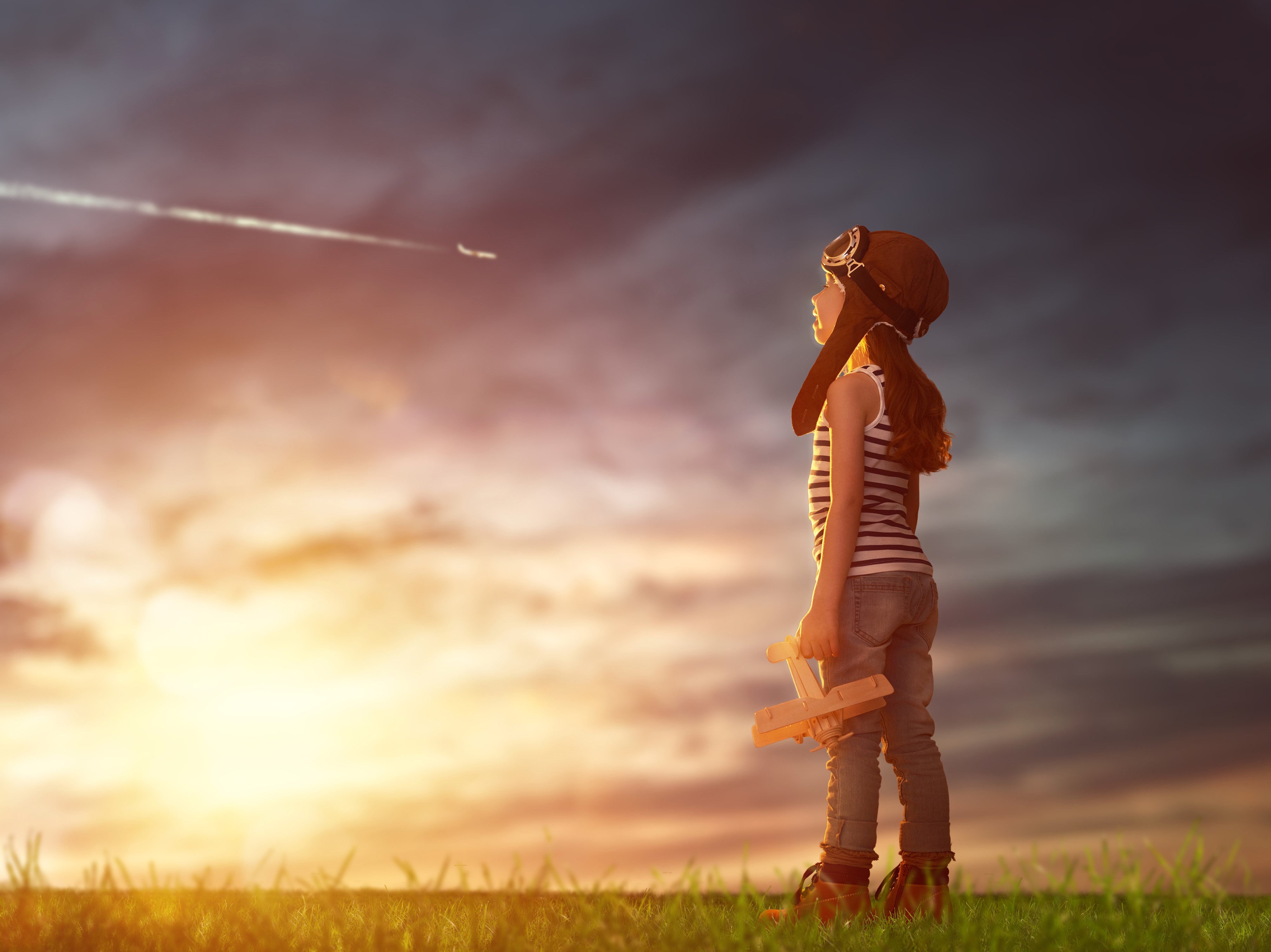 Girl in pilot helmet with toy airplane watching a jet HD Wallpaper