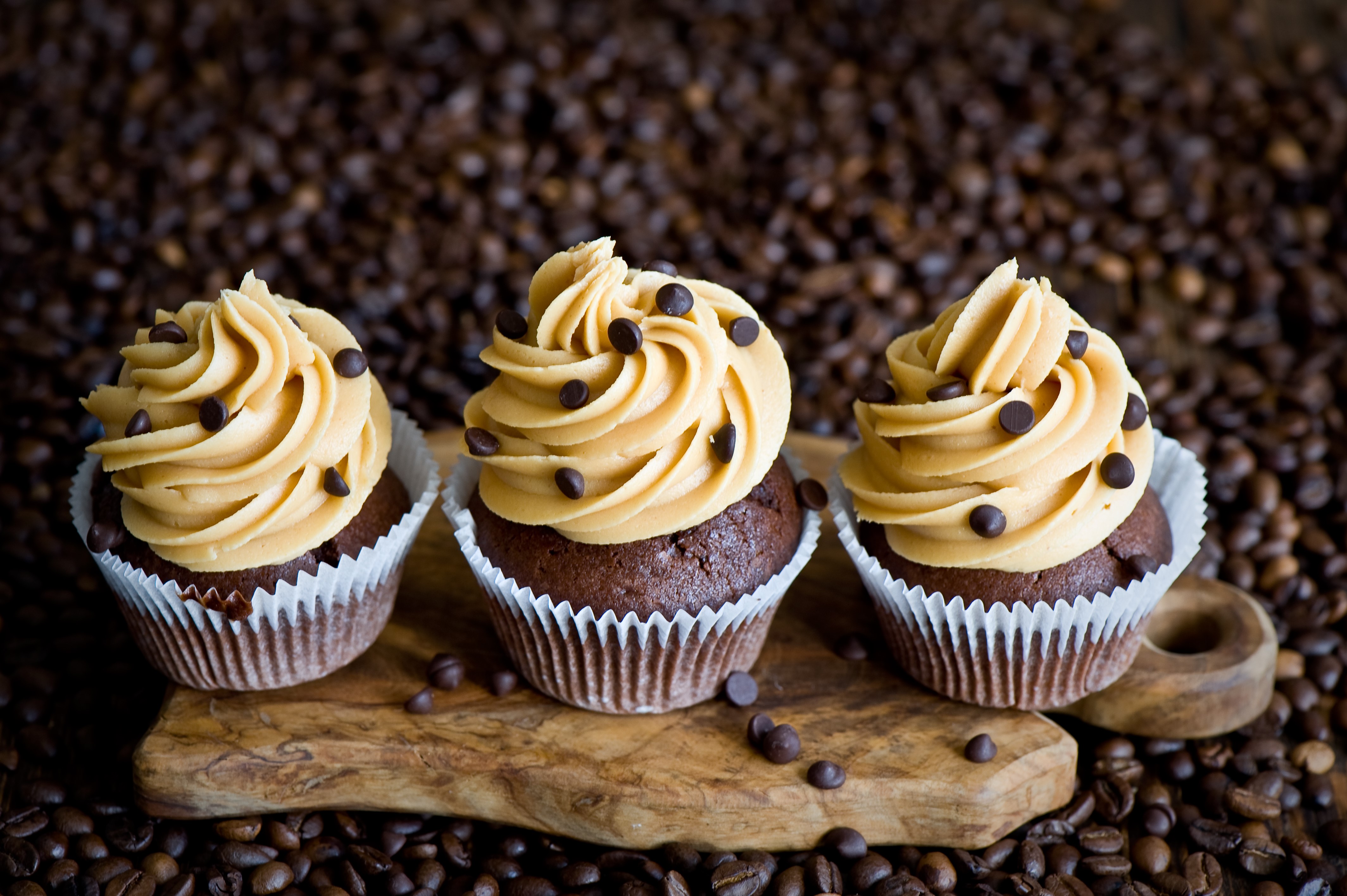 Three chocolate cupcakes with peanut butter frosting and chocolate chips on a cutting board surrounded by coffee beans HD Wallpaper