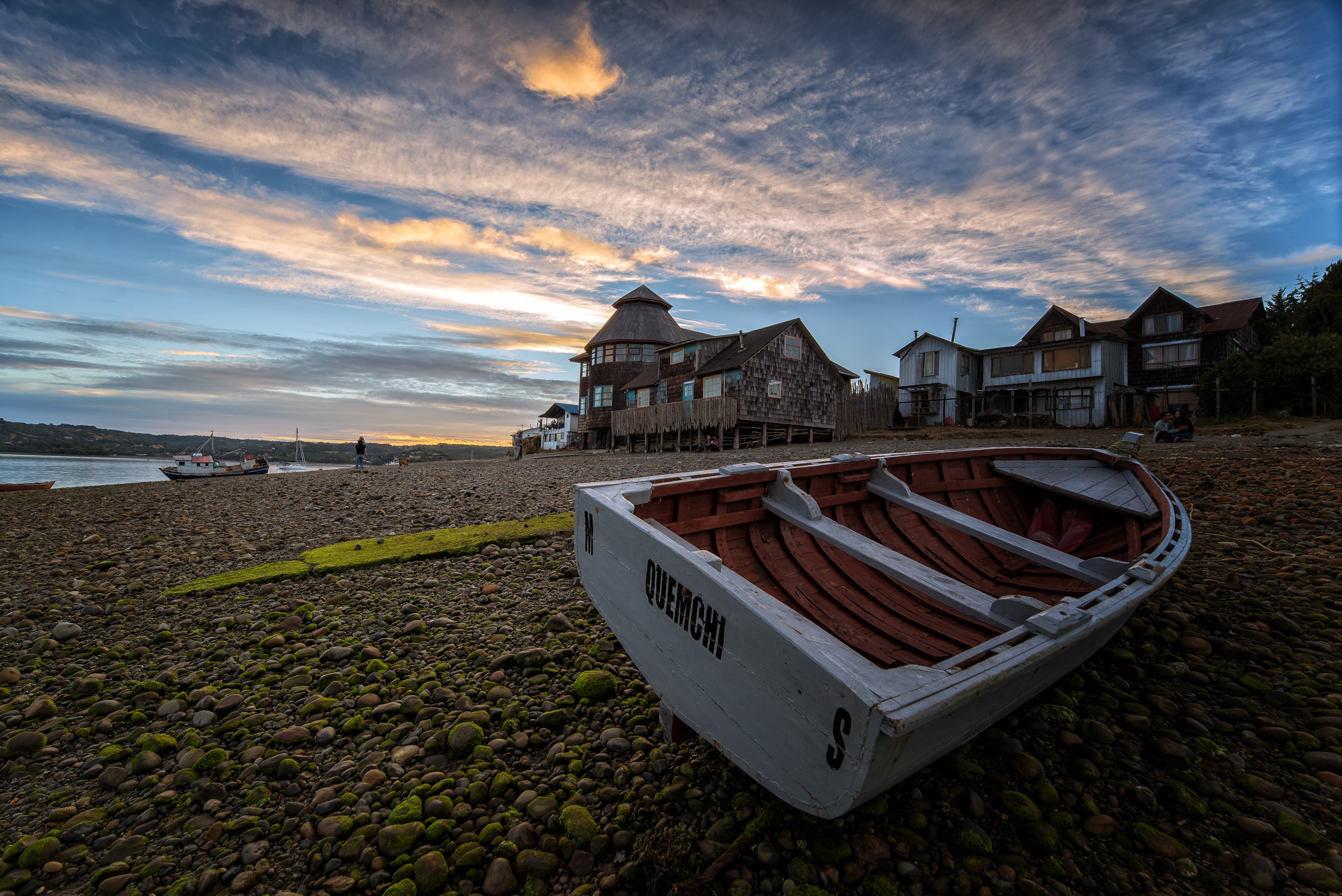Boat on a rocky shore with houses and sunset sky HD Wallpaper