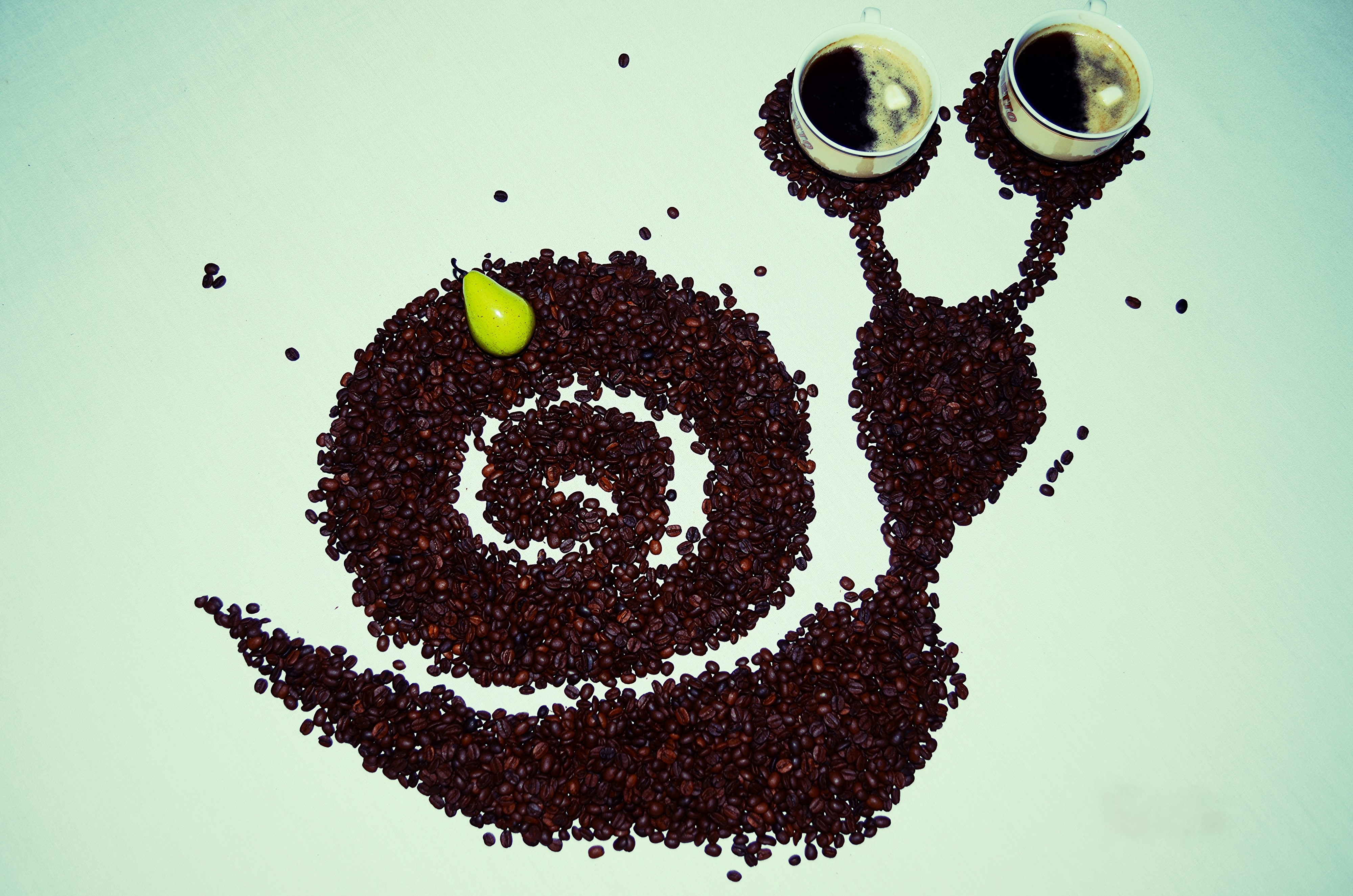 Coffee beans arranged as a snail with cups and a pear HD Wallpaper