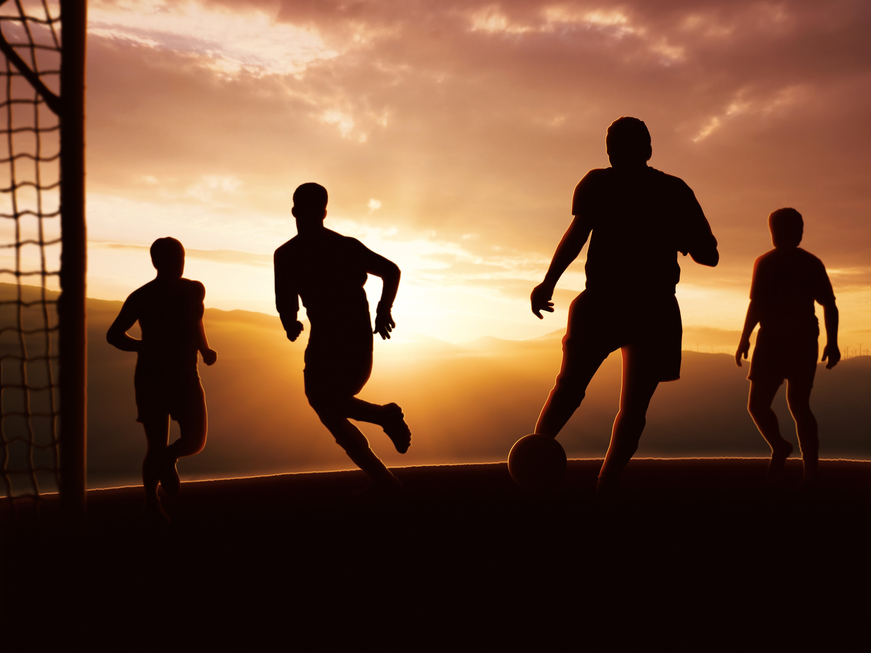 Silhouettes of men playing soccer at sunset HD Wallpaper