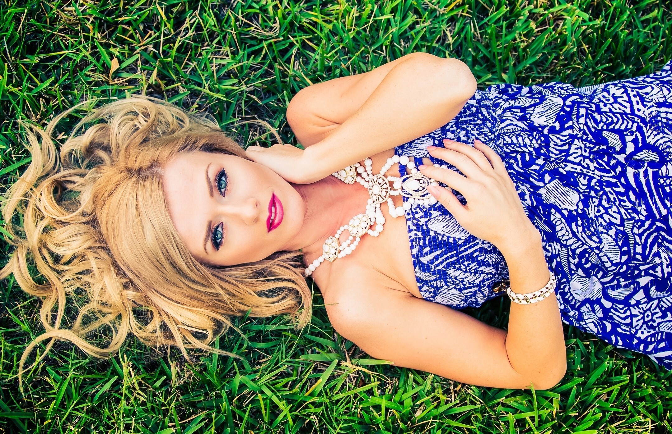 Blonde woman lying on grass wearing blue dress and jewelry HD Wallpaper