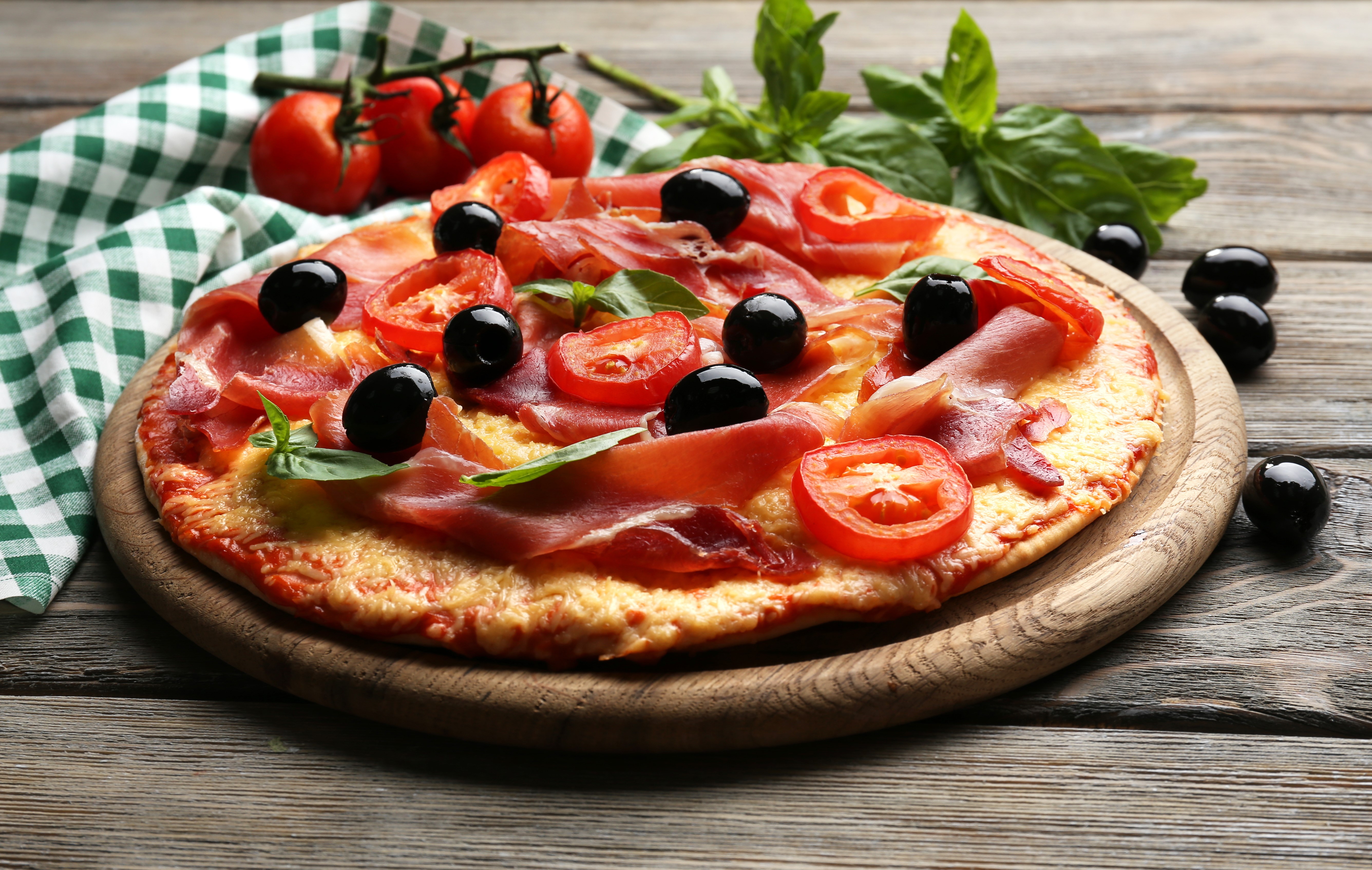 Pizza with prosciutto, tomatoes, and olives on a wooden board HD Wallpaper