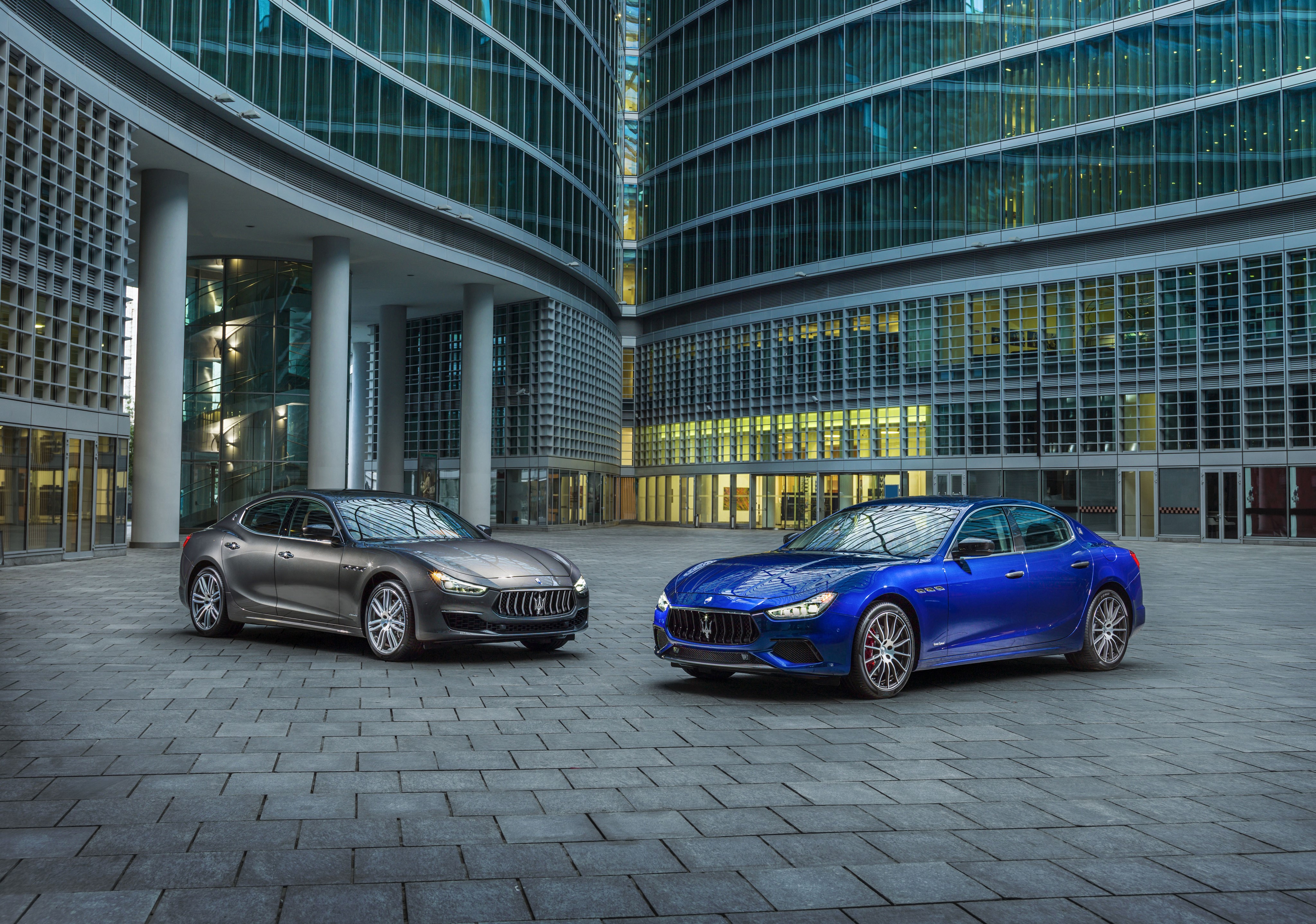 Two Maserati Ghibli cars parked outside modern buildings HD Wallpaper