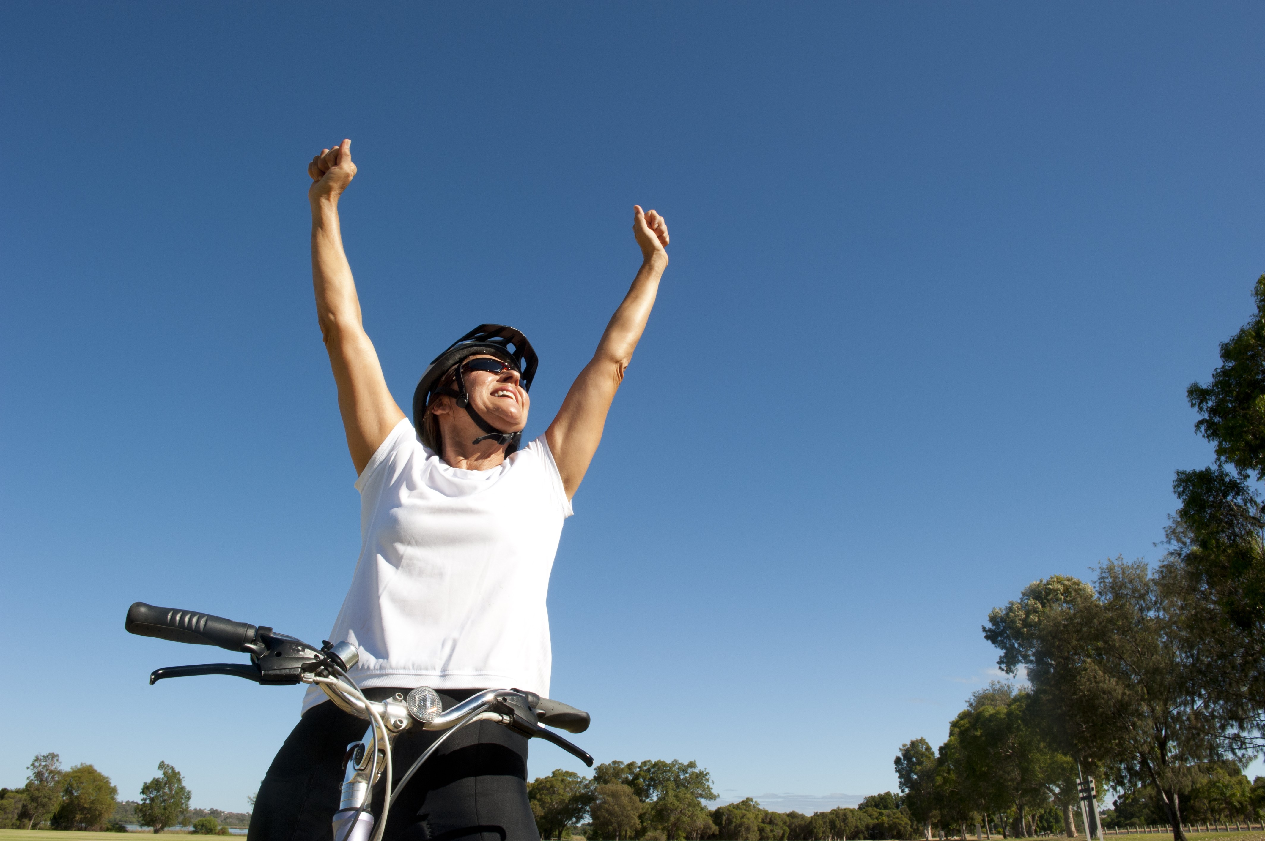 Woman on bicycle with arms raised in celebration HD Wallpaper