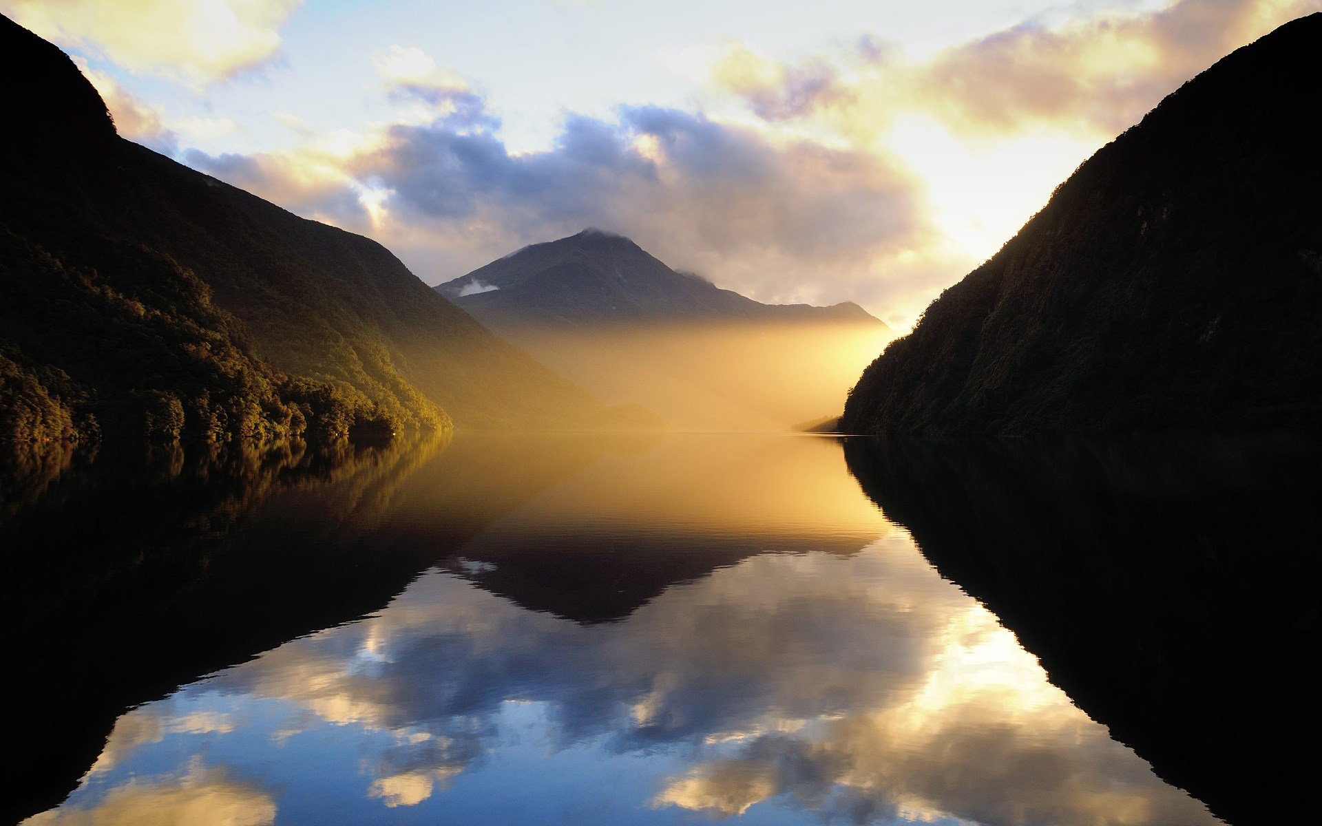 Misty mountains reflected in a calm lake at sunrise HD Wallpaper