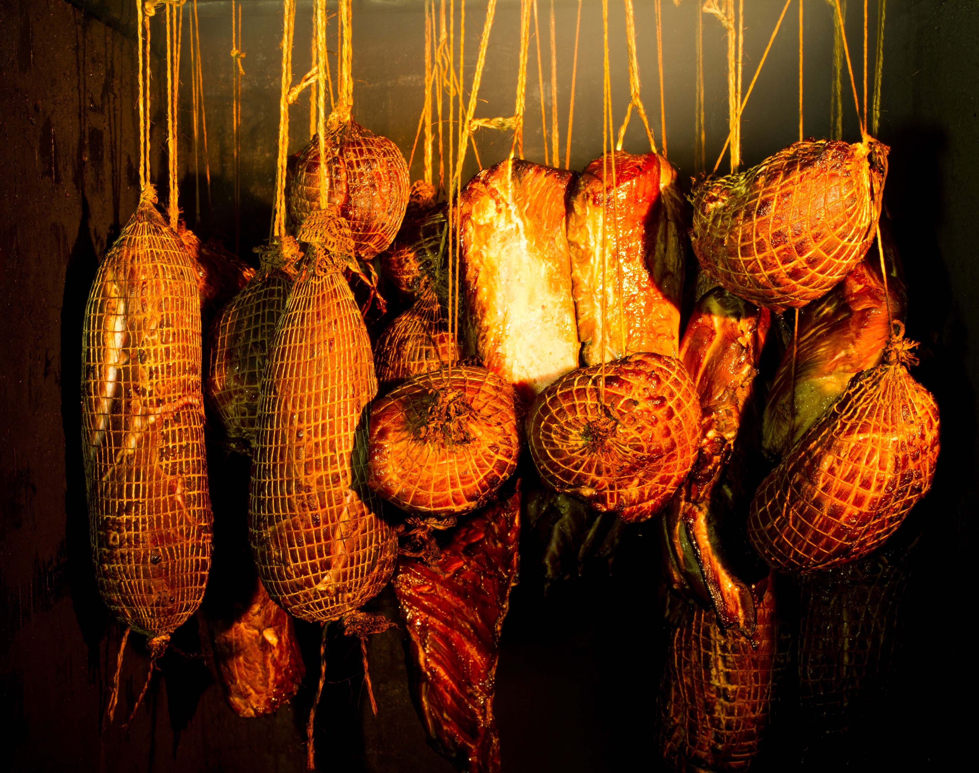 Smoked meat products hanging in a dark room HD Wallpaper