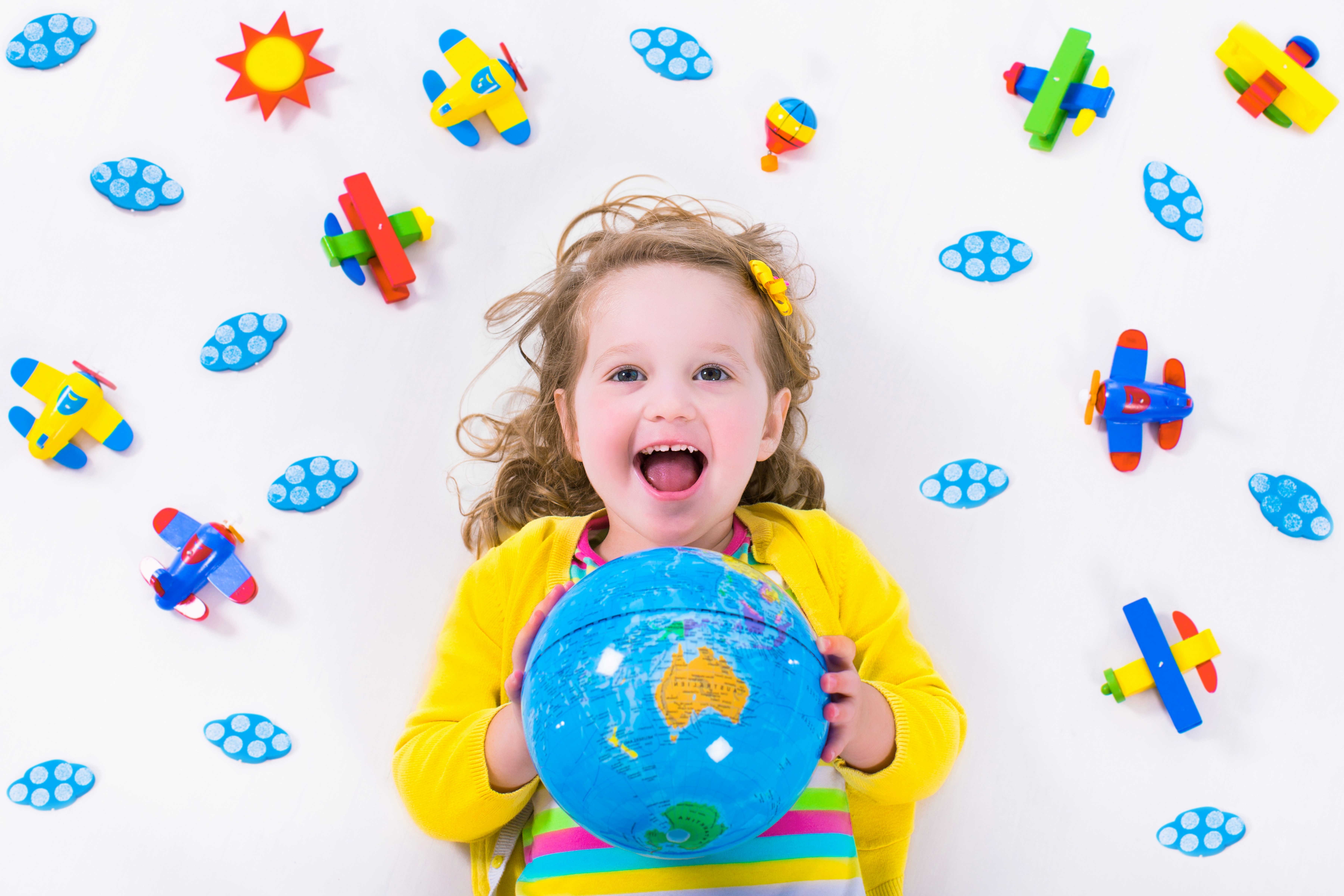 Little girl holding a globe surrounded by toy airplanes and clouds HD Wallpaper