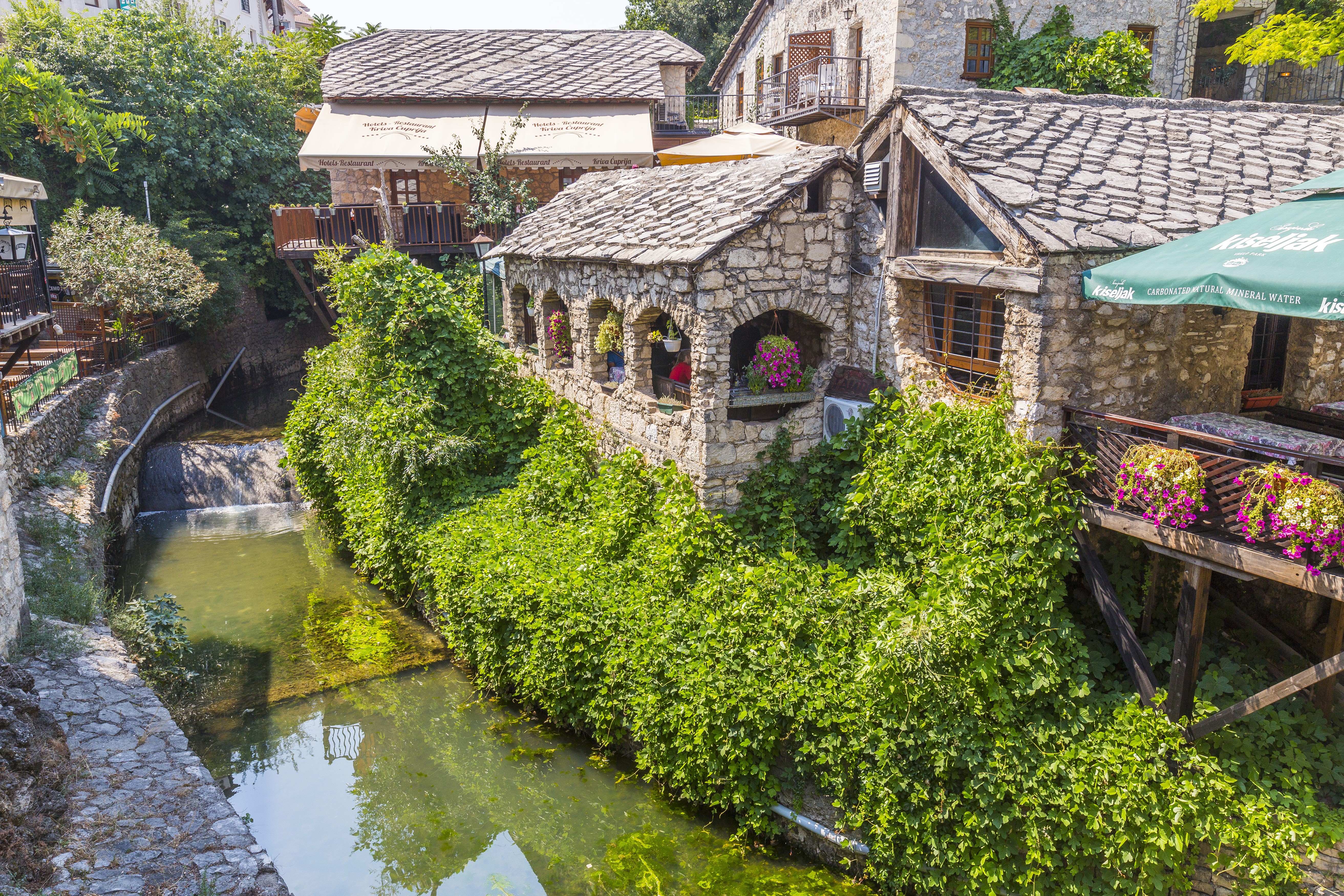 Mostar, Bosnia and Herzegovina: Stone houses by a river with lush greenery HD Wallpaper