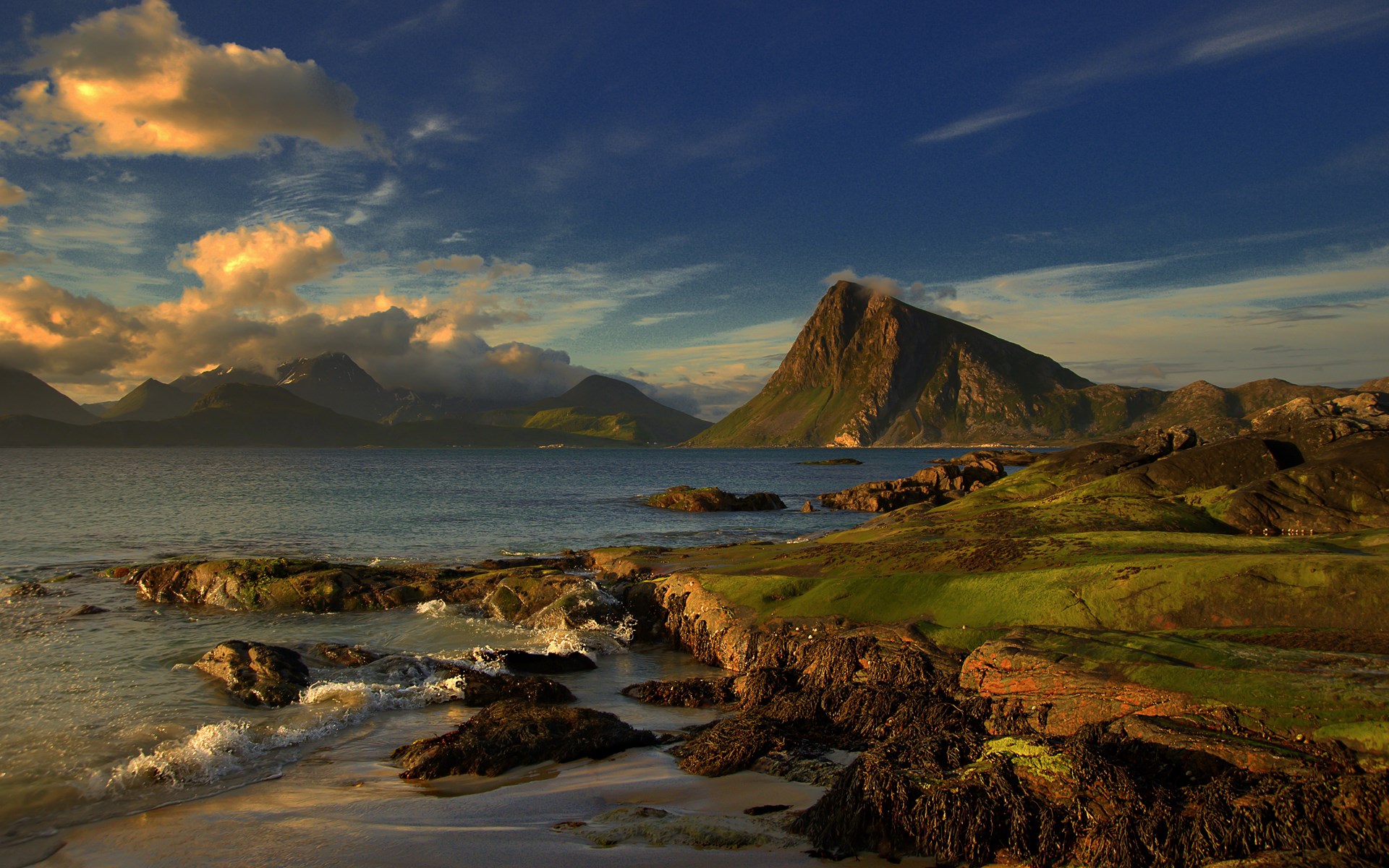 Rocky coastline with mountains and ocean under a cloudy sky HD Wallpaper