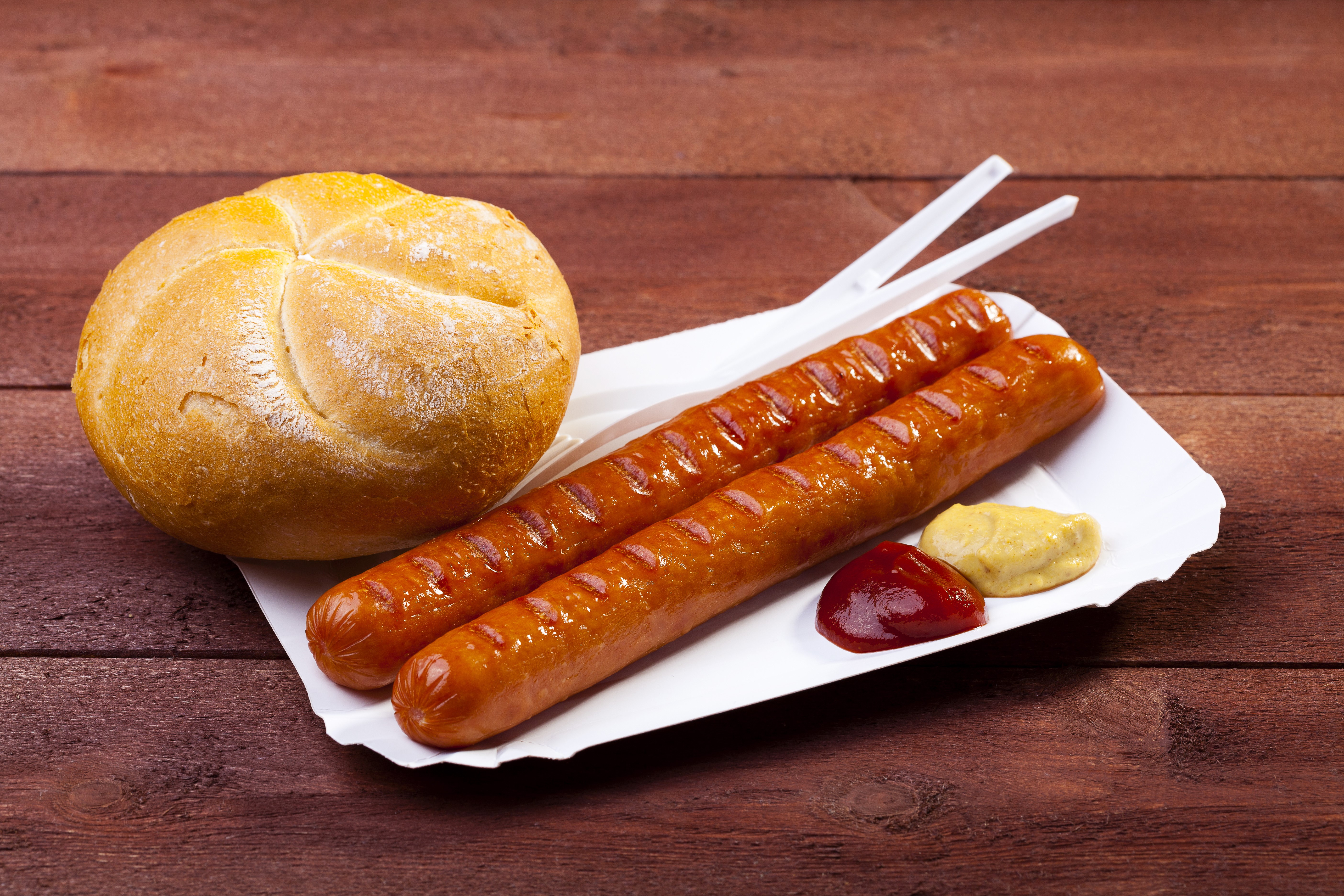 Two sausages with a bun and condiments on a wooden table HD Wallpaper