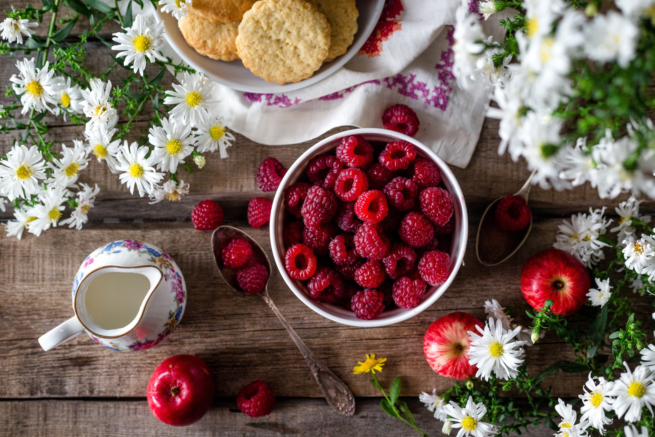 Raspberries, apples, cookies, and flowers on a wooden table HD Wallpaper
