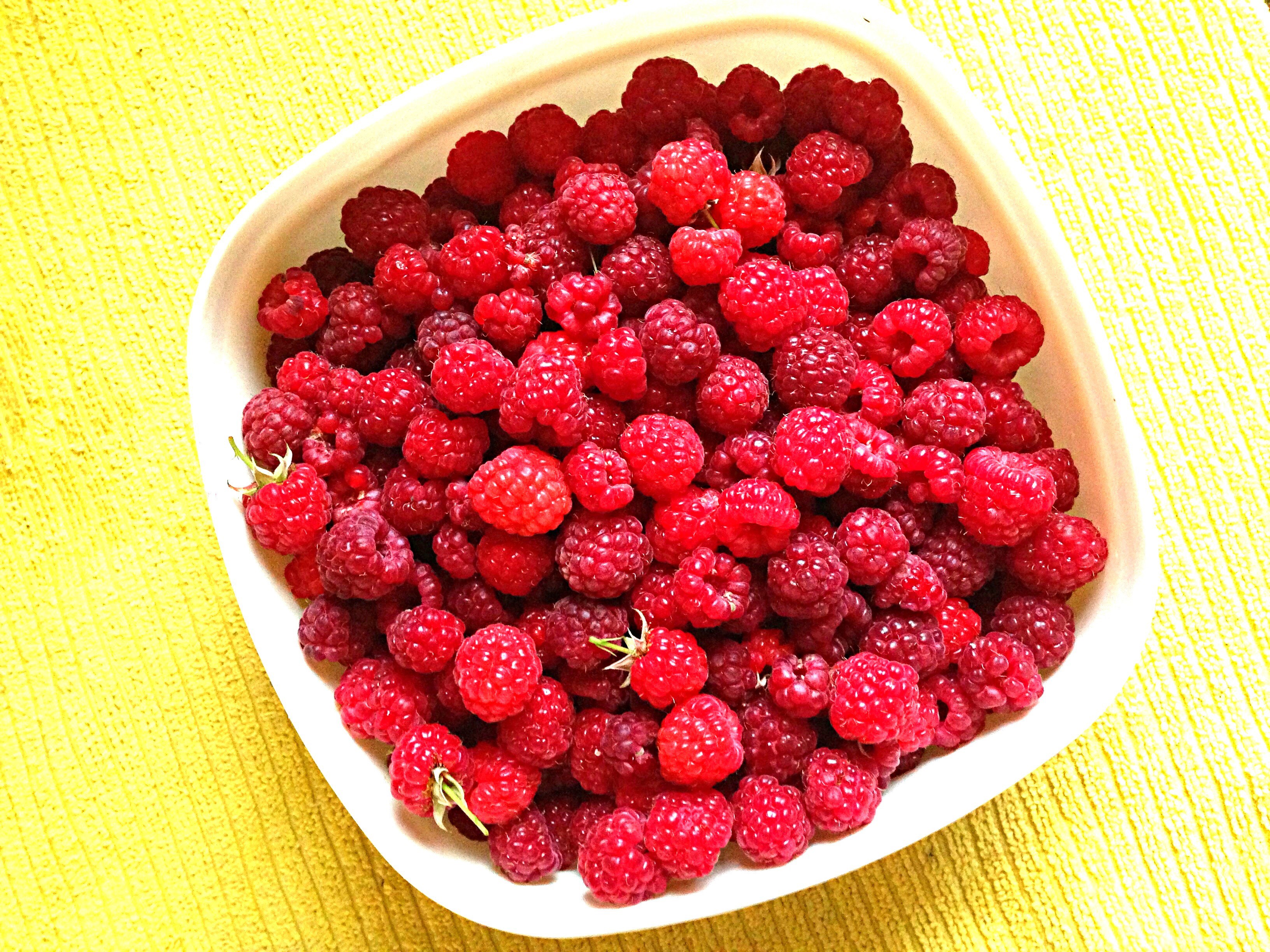 Bowl of fresh raspberries on a yellow surface HD Wallpaper
