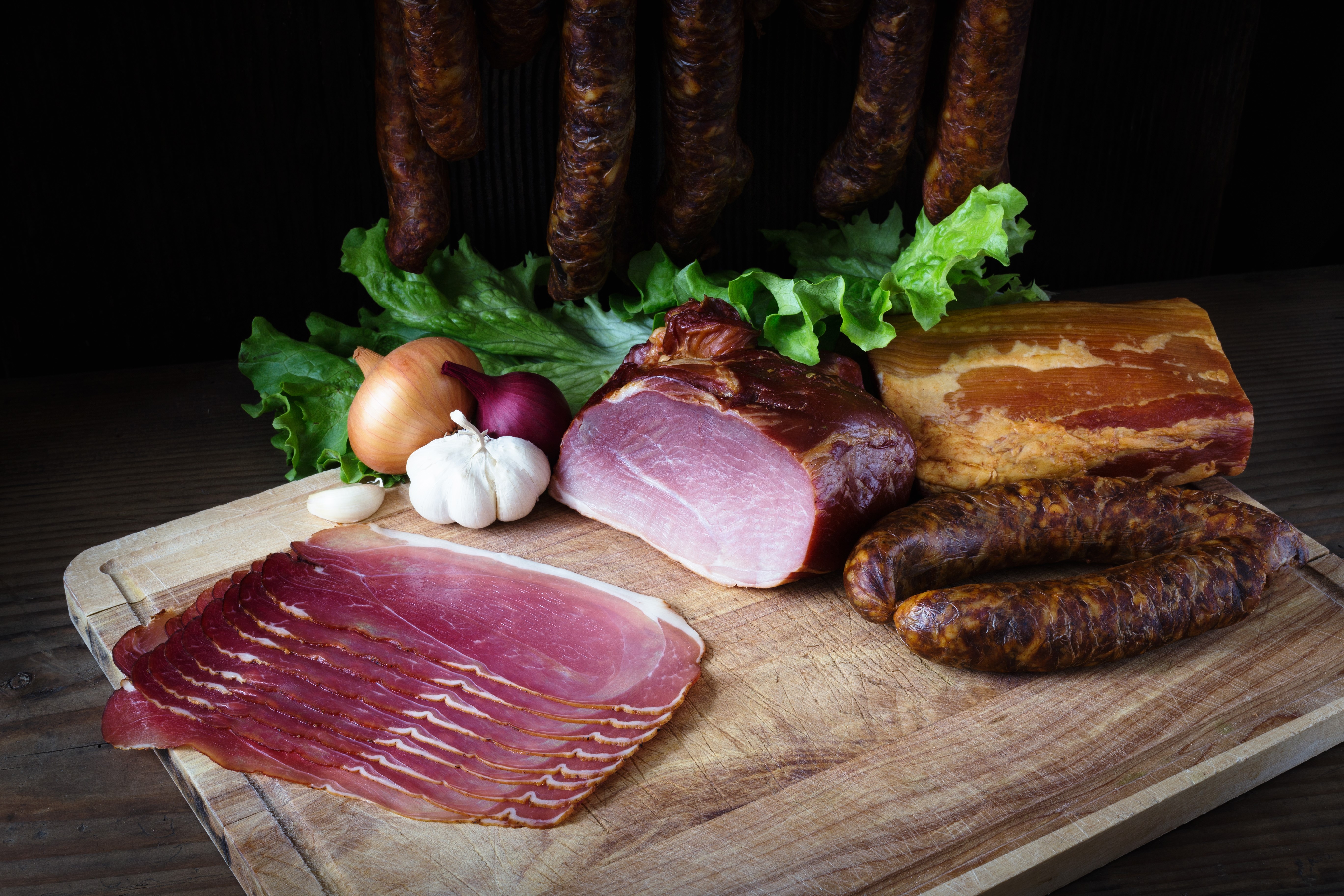 Meat products, sausage, ham, onion, garlic, and lettuce on a cutting board HD Wallpaper
