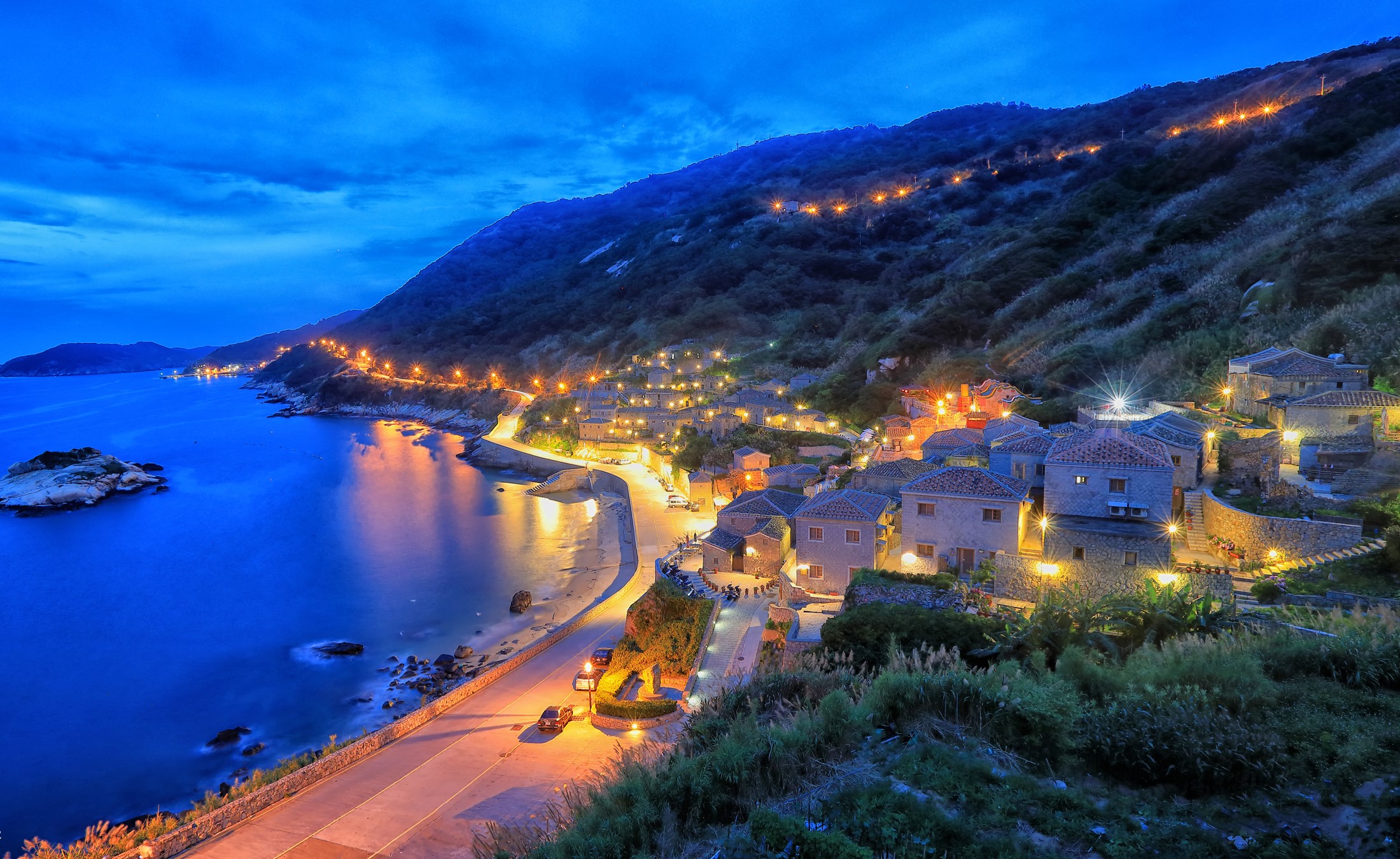 Coastal village at dusk with illuminated houses on a hillside in Taiwan HD Wallpaper