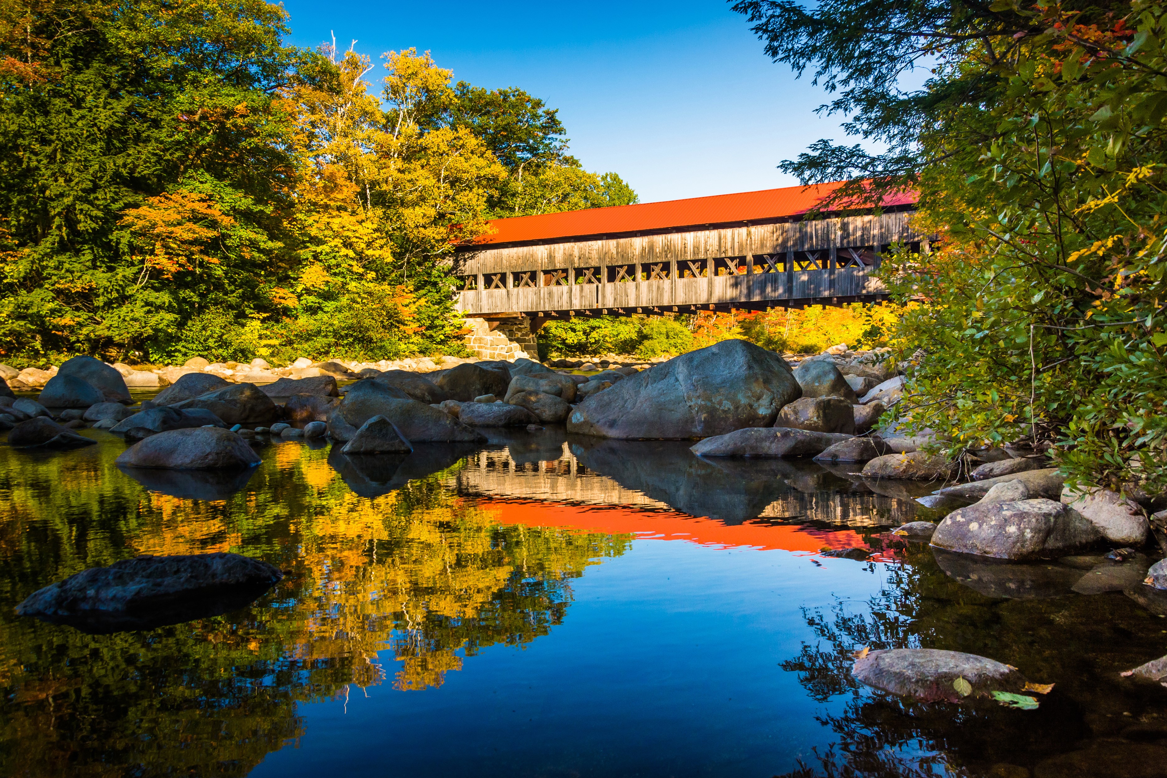 Covered bridge over river with autumn foliage and rocks HD Wallpaper