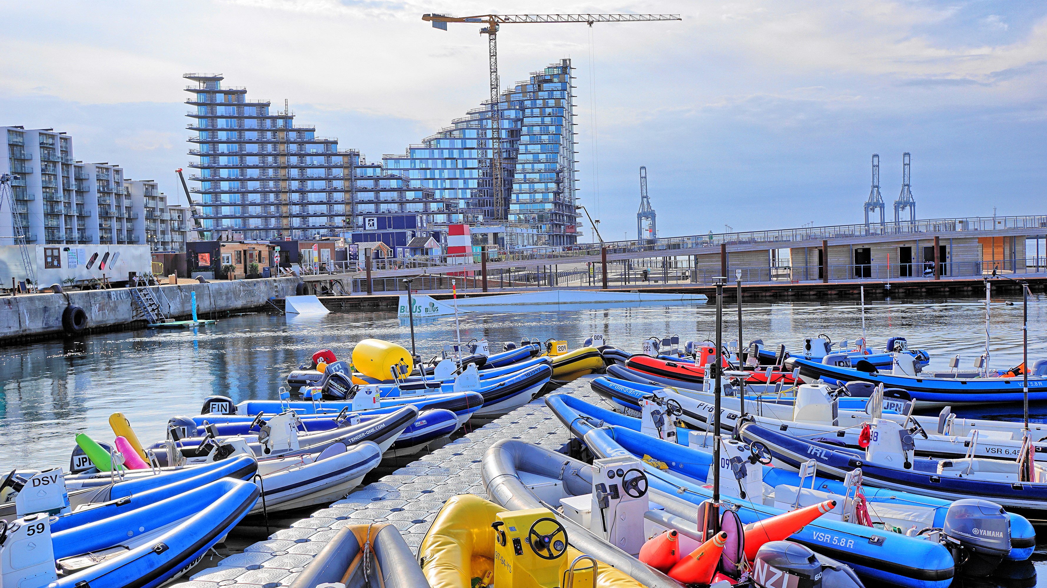 Boats docked at a marina with modern buildings and cranes in the background HD Wallpaper