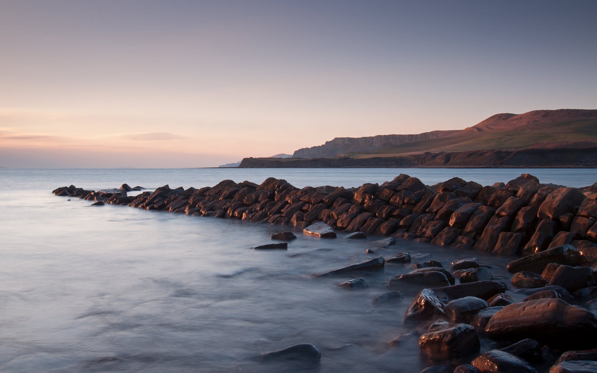 Rocky coastline at sunset with calm sea HD Wallpaper
