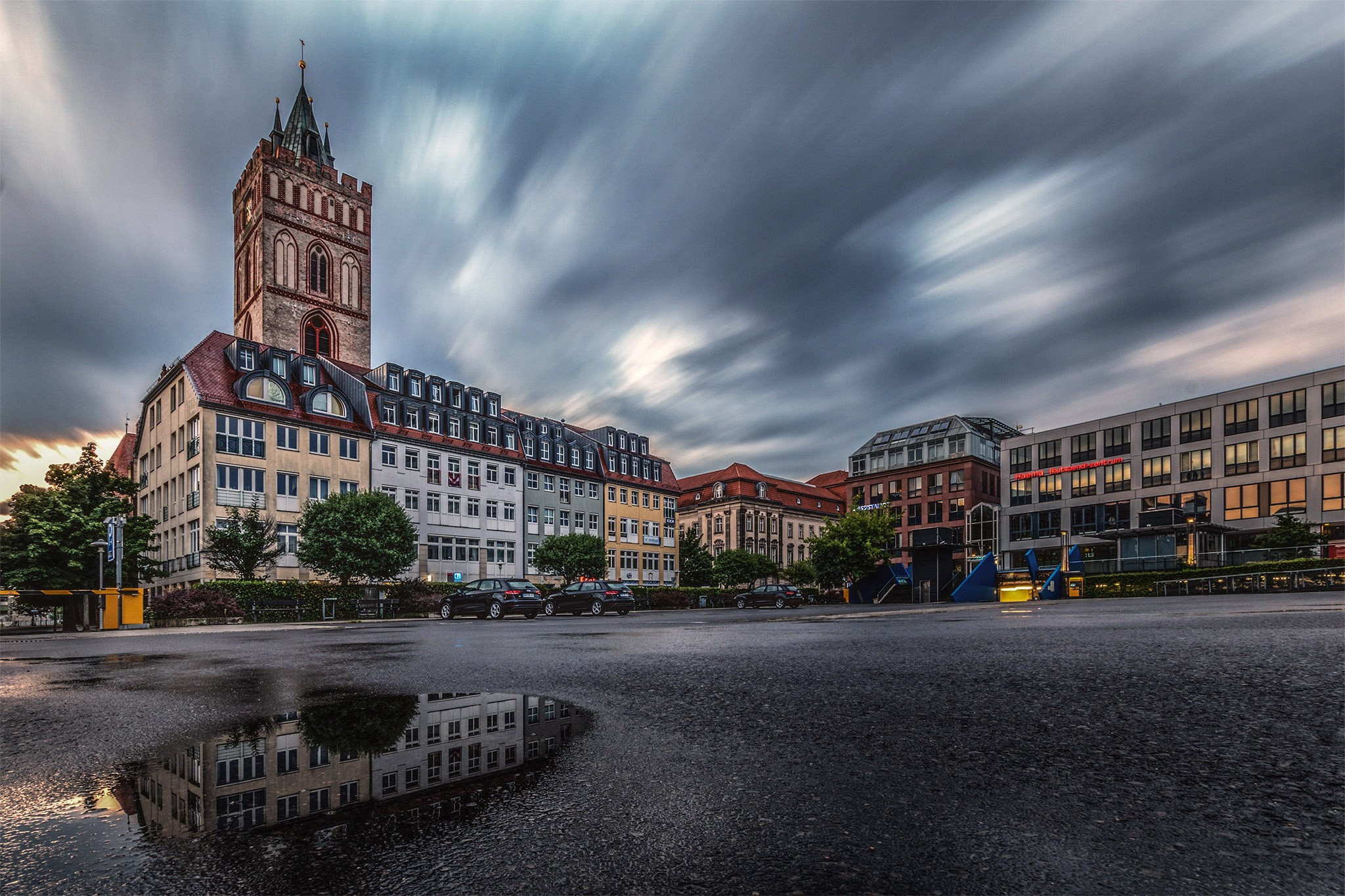 Town square with church tower and reflection in puddle HD Wallpaper