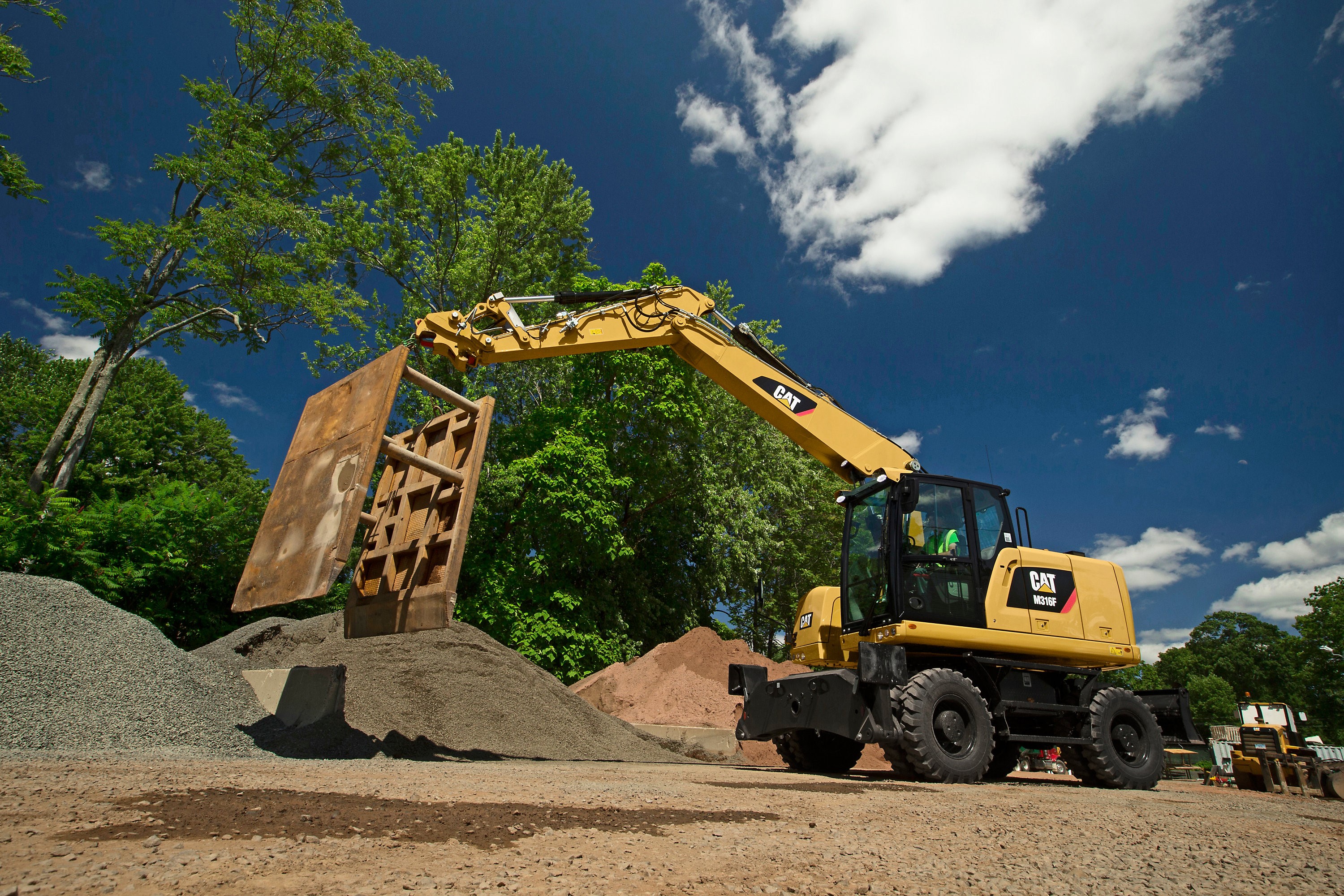 Caterpillar M316F Wheeled Excavator Moving a Large Panel HD Wallpaper