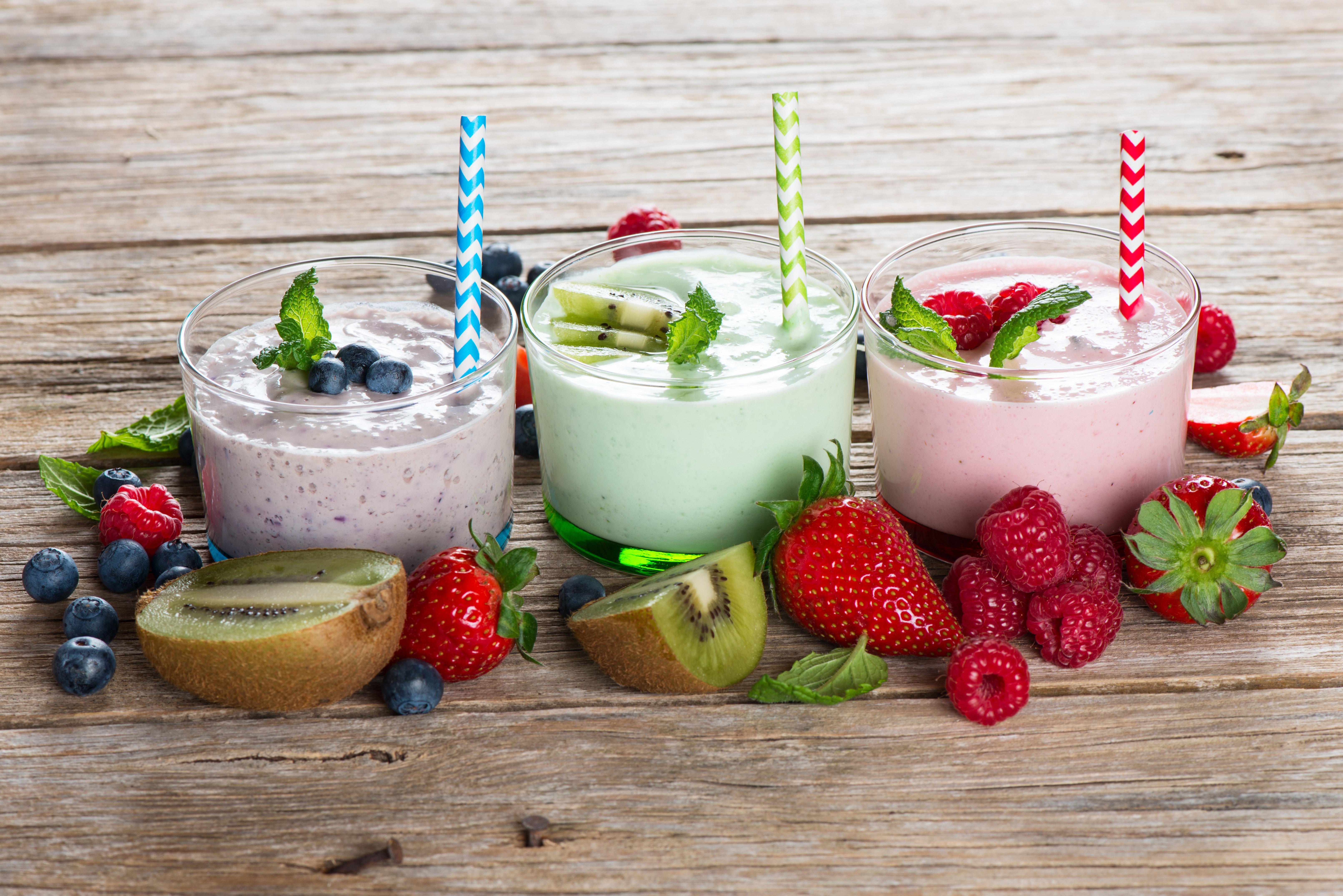 Three fruit smoothies with strawberries, blueberries, and kiwi on wood HD Wallpaper